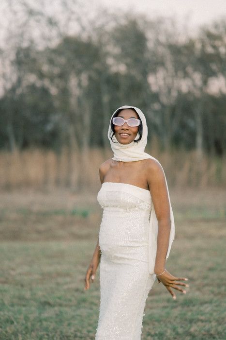 Joyful maternity portrait featuring woman in strapless white dress and sunglasses outdoors.