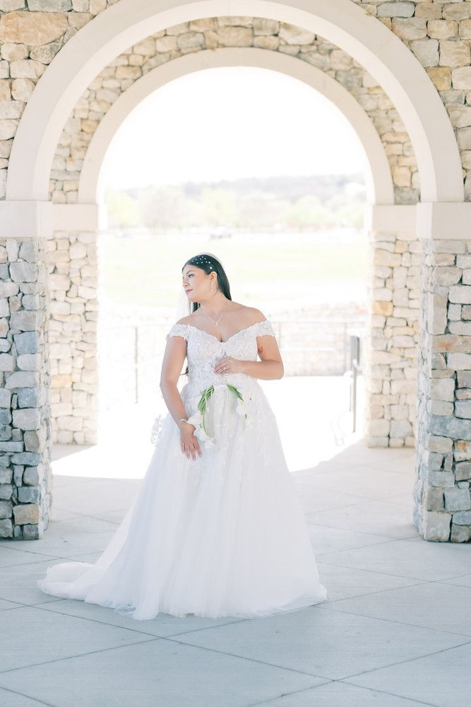 Romantic wedding photography featuring a flowing white gown in a light-filled stone archway.
