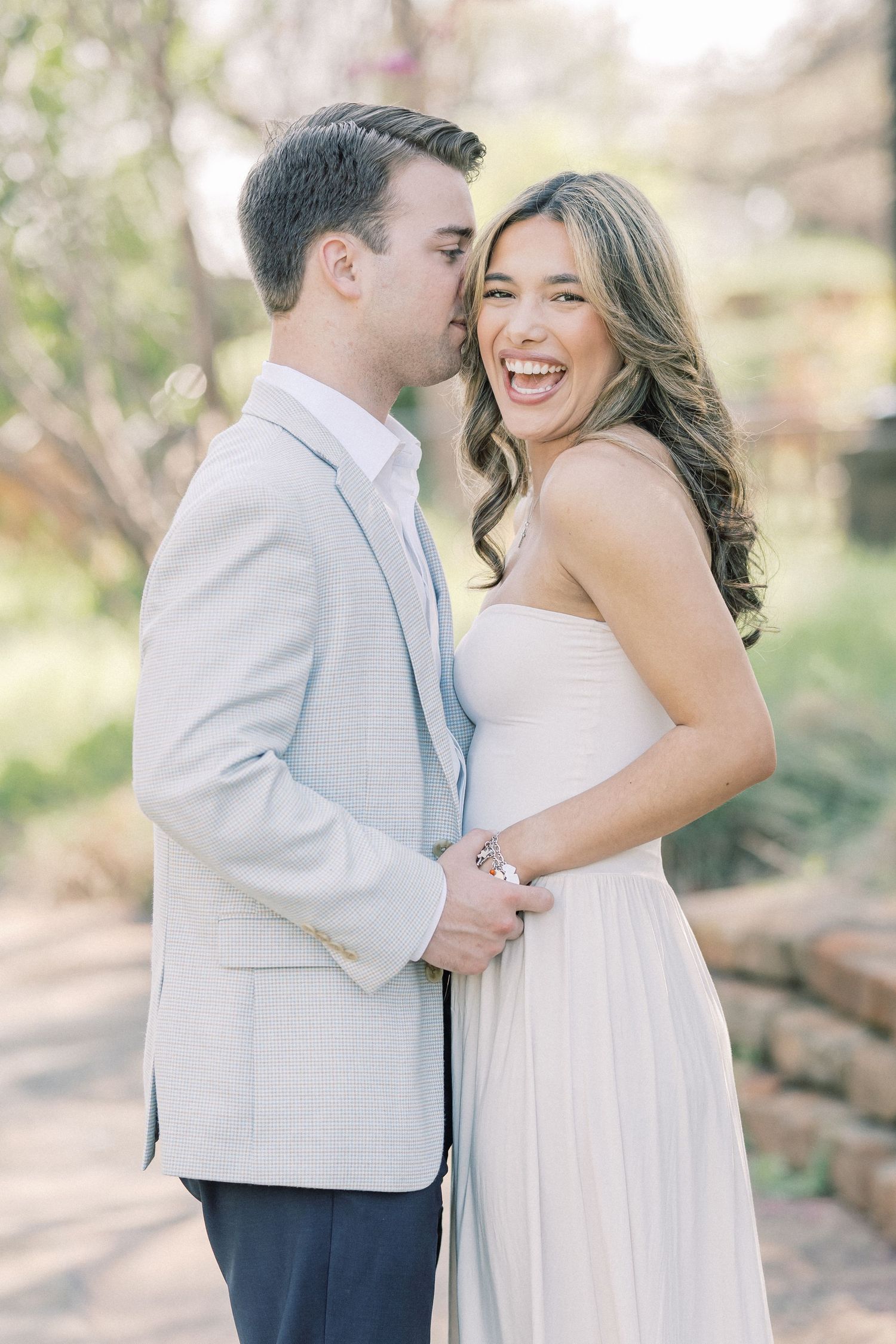 A couple shares romantic moments in a natural outdoor setting wearing white and blue formal attire.