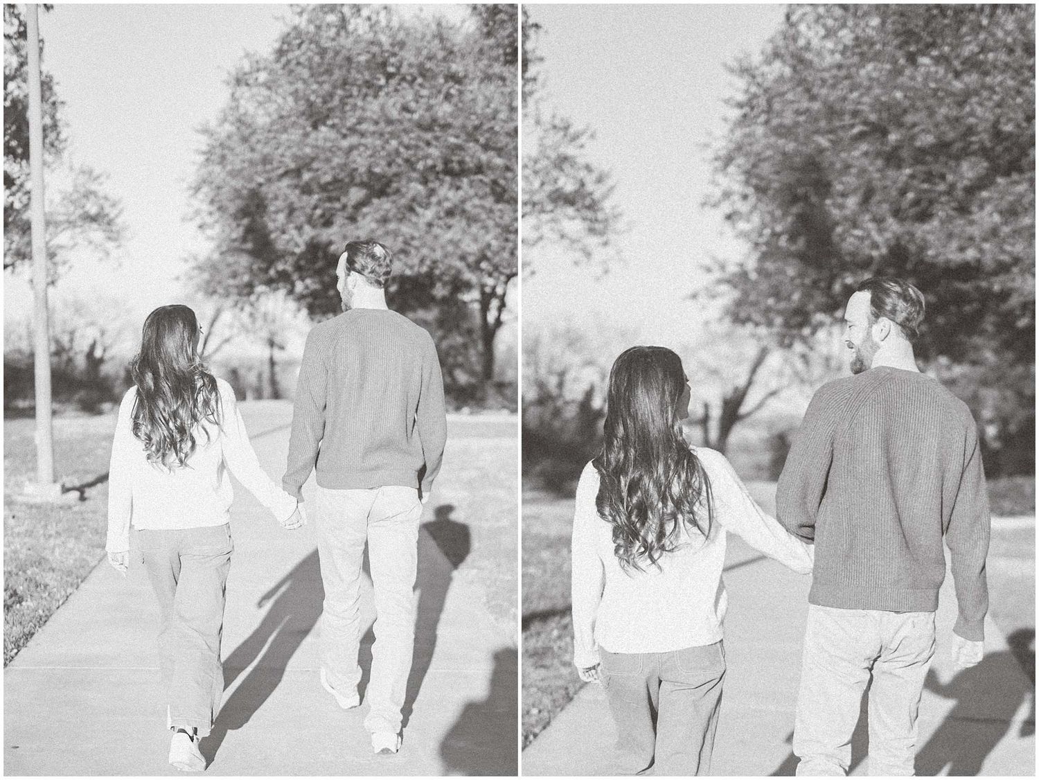 Black and white photo of a couple walking together on a path under trees holding hands from behind.