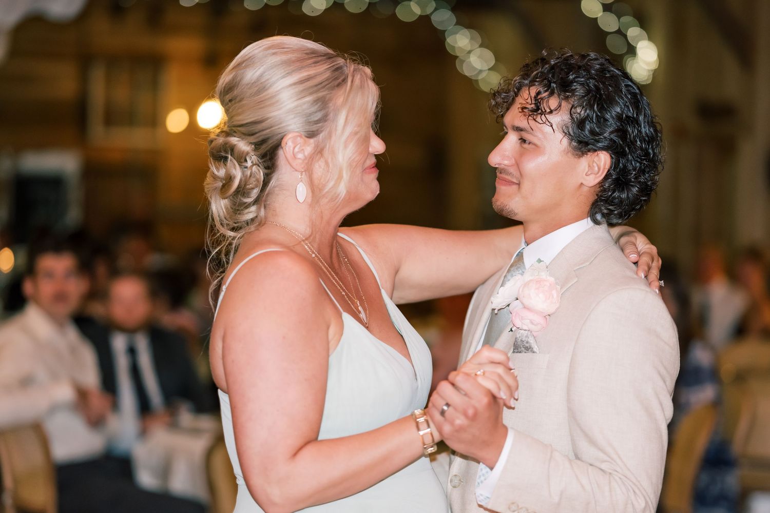 Bride and groom sharing first dance at wedding reception, bride in sage dress with arm around groom in beige suit.