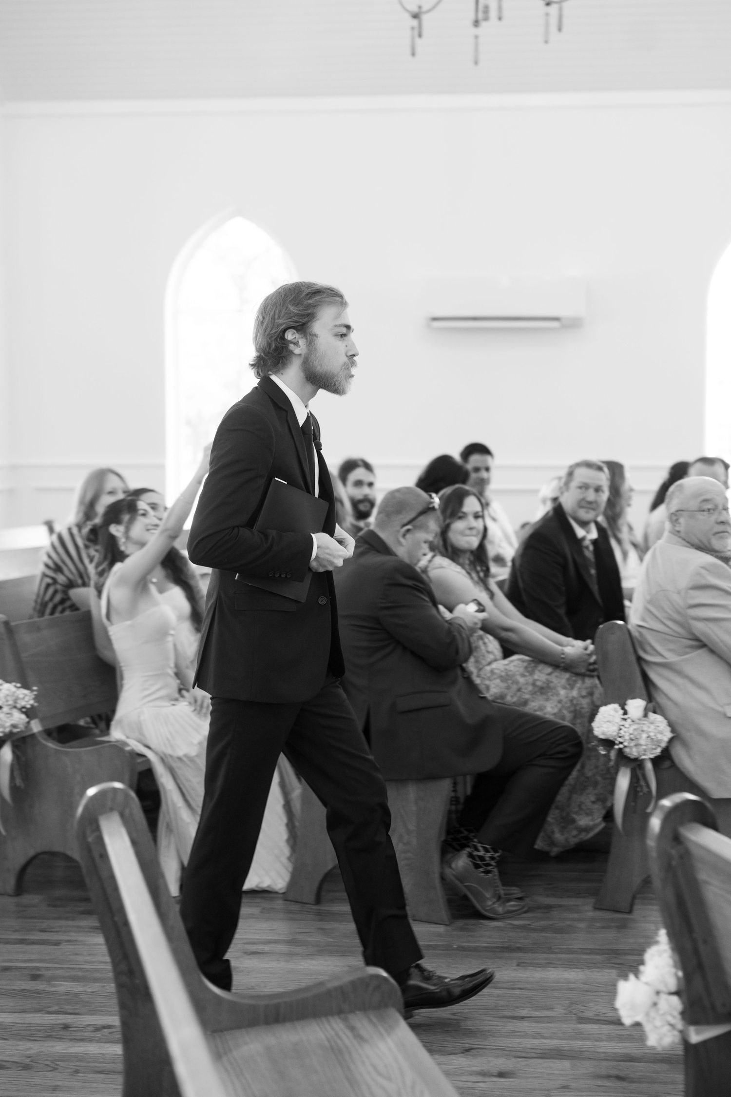 Black and white photo of groomsman walking down church aisle during ceremony.