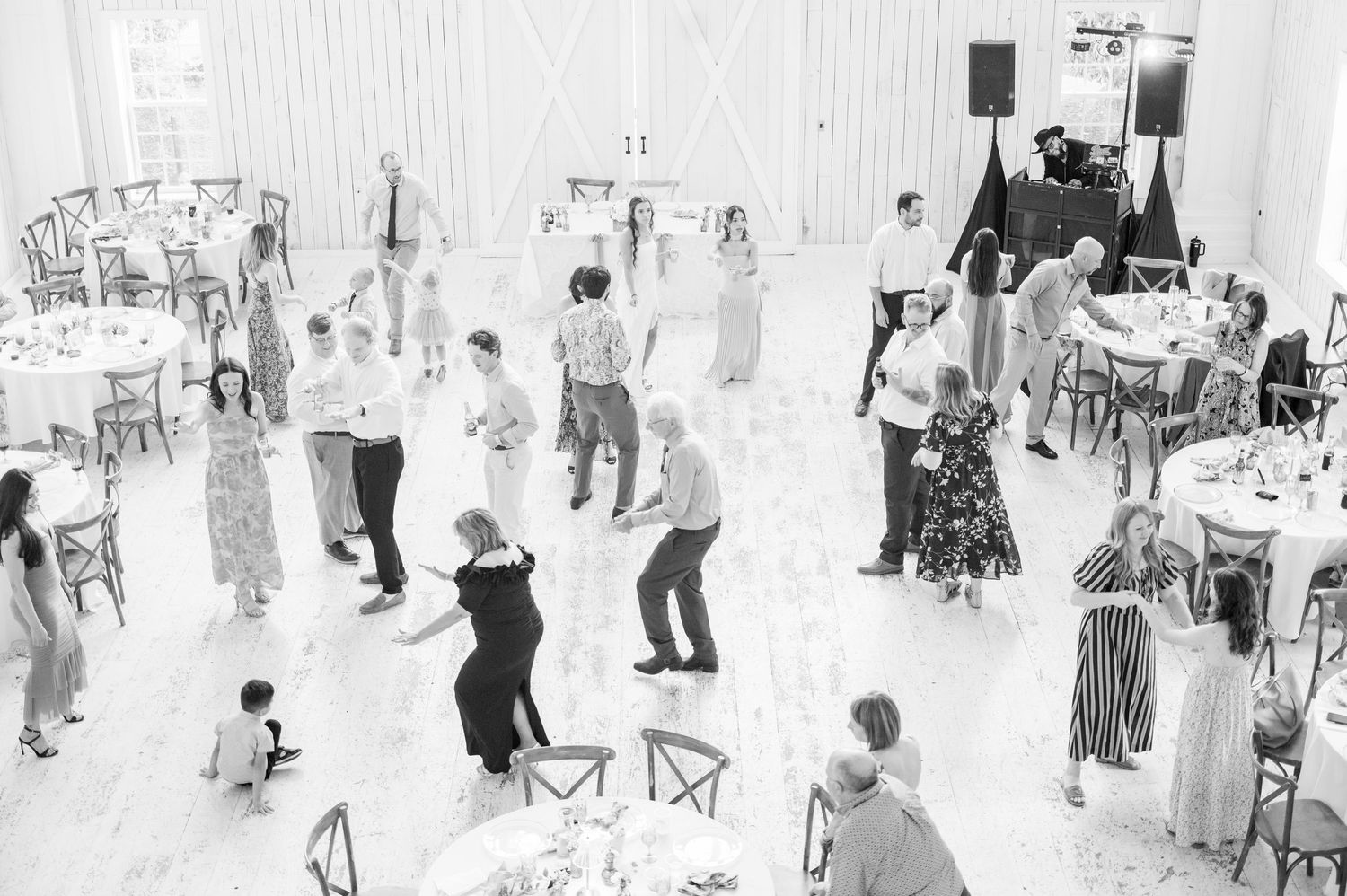 Black and white aerial view of wedding guests dancing on a white floor in a decorated barn reception.