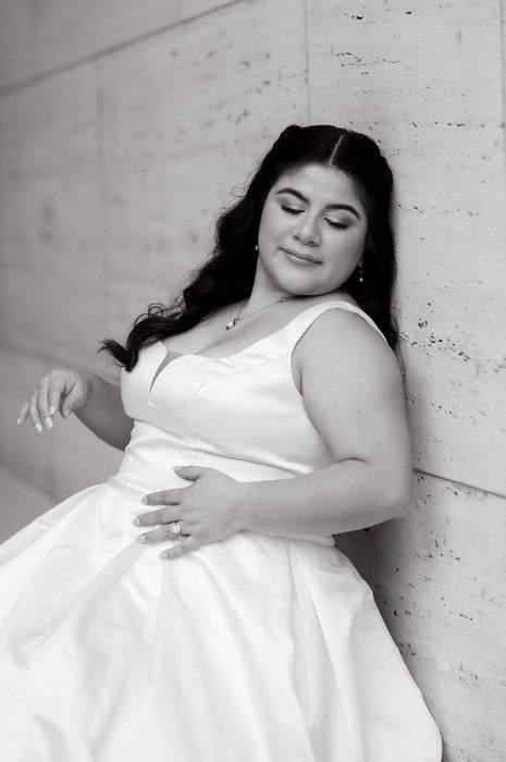 Black and white portrait of bride in white gown leaning against concrete wall with eyes closed.