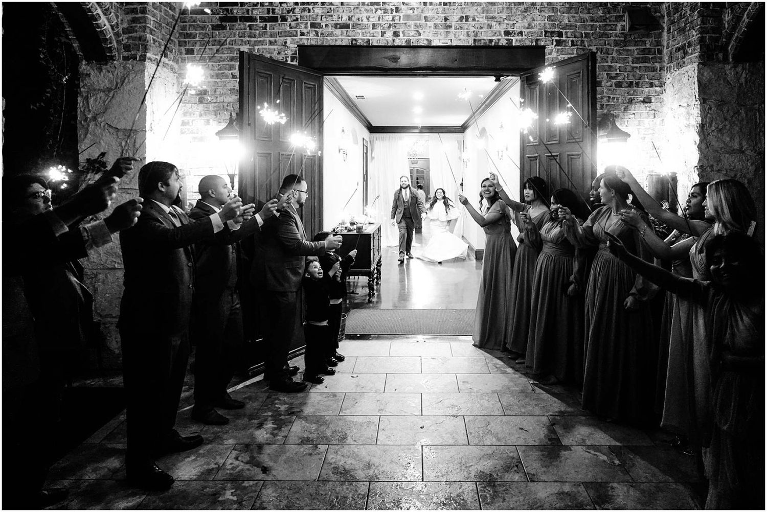 Black and white photo of bride and groom making grand entrance through doors lined with cheering wedding guests.