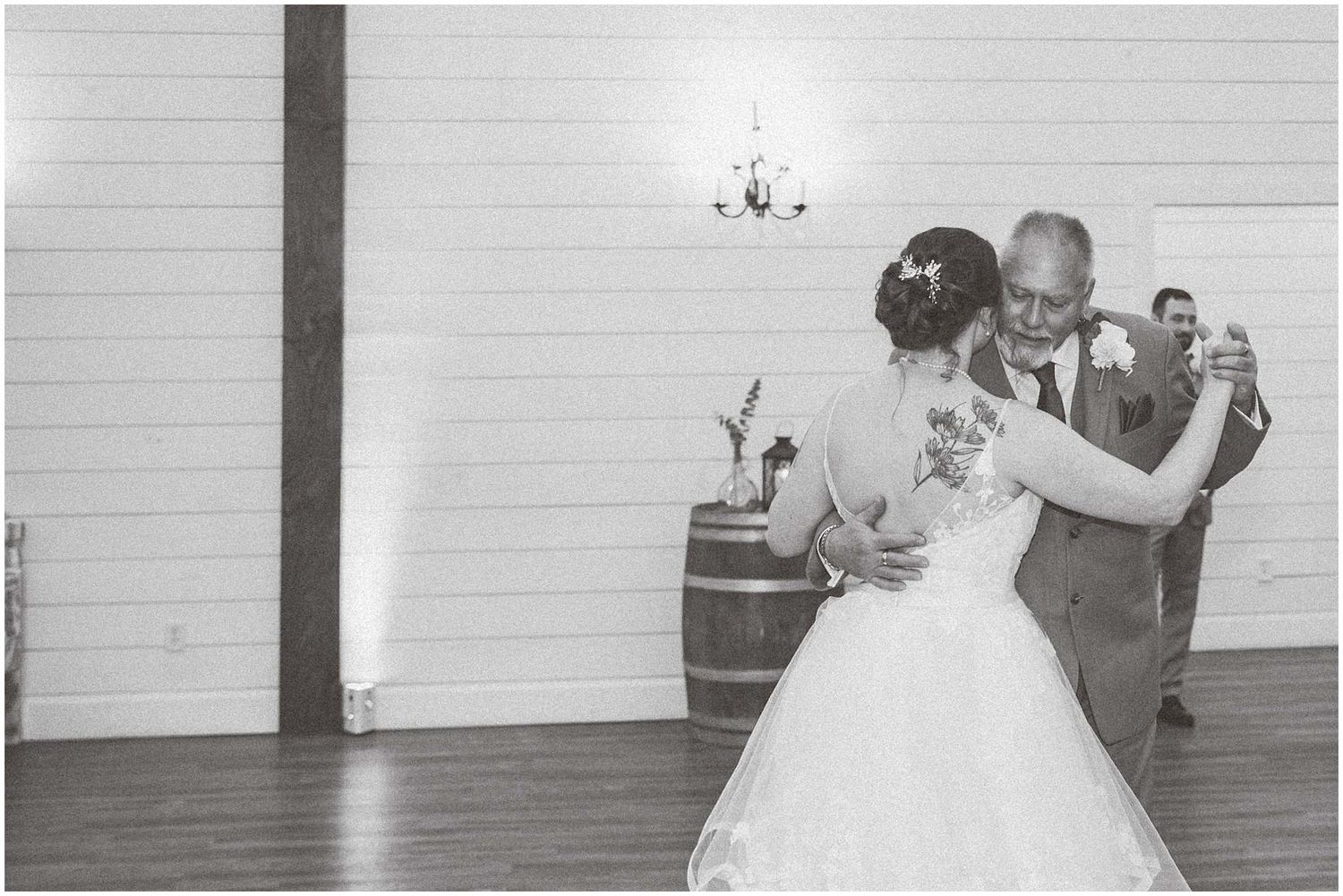 A couple performs their first dance at a wedding reception in a white-walled venue with onlookers in the background.