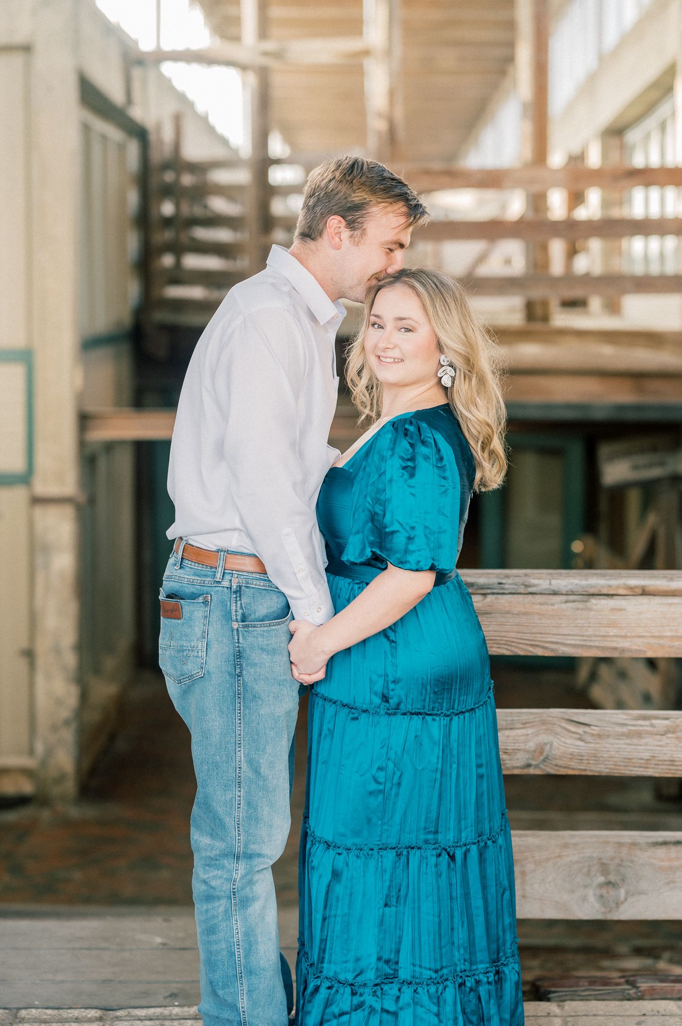 A couple shares an intimate moment on wooden stairs with the woman wearing a striking teal tiered dress.