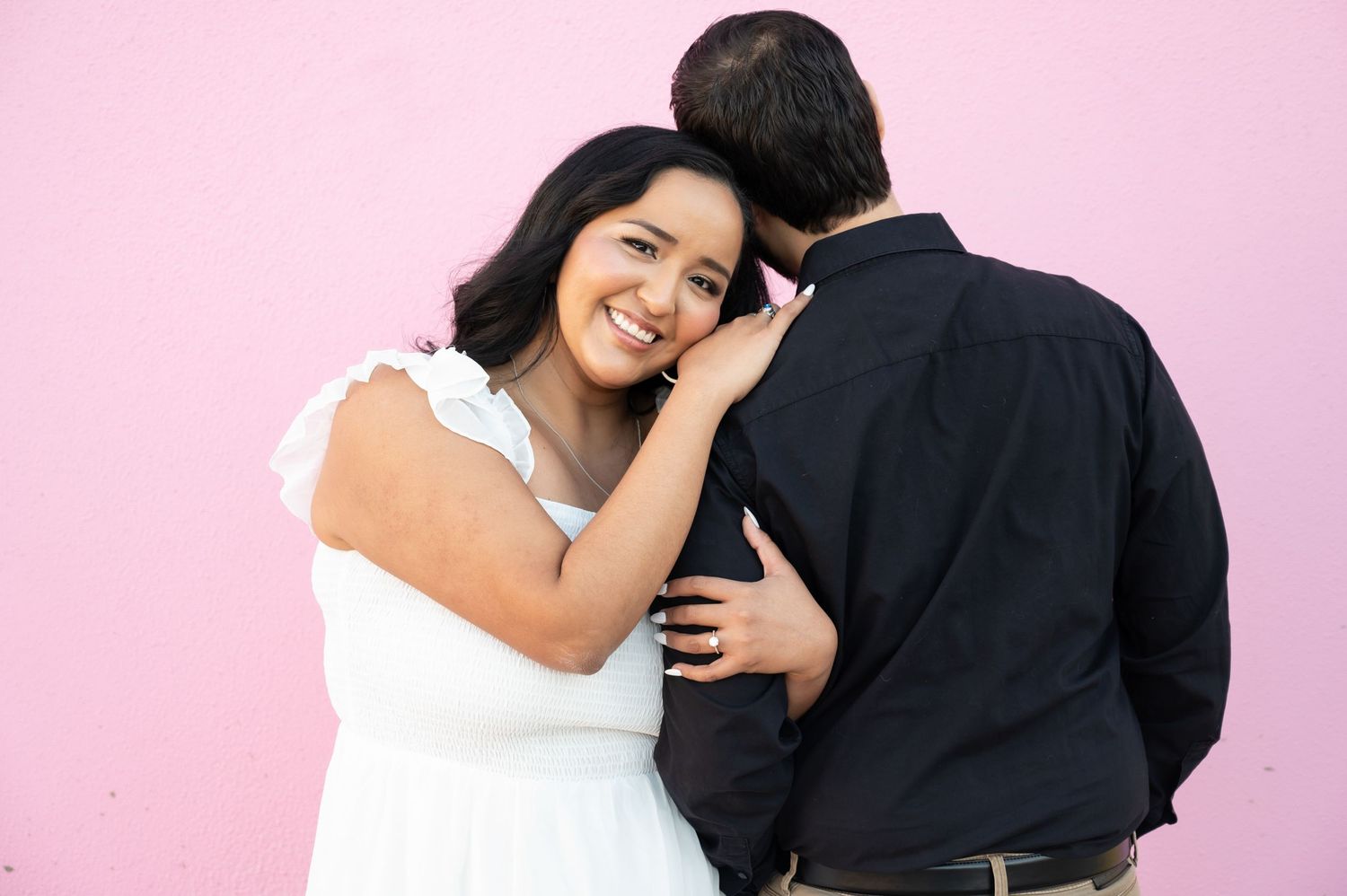 A romantic couple embraces against a pink wall while wearing contrasting white and black outfits.