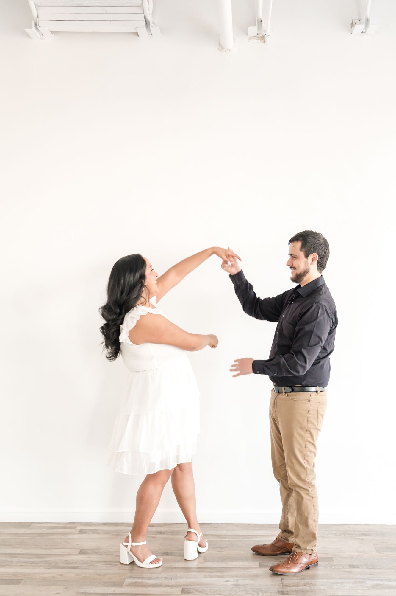 Couple dancing together in bright studio with white walls and wooden floors.
