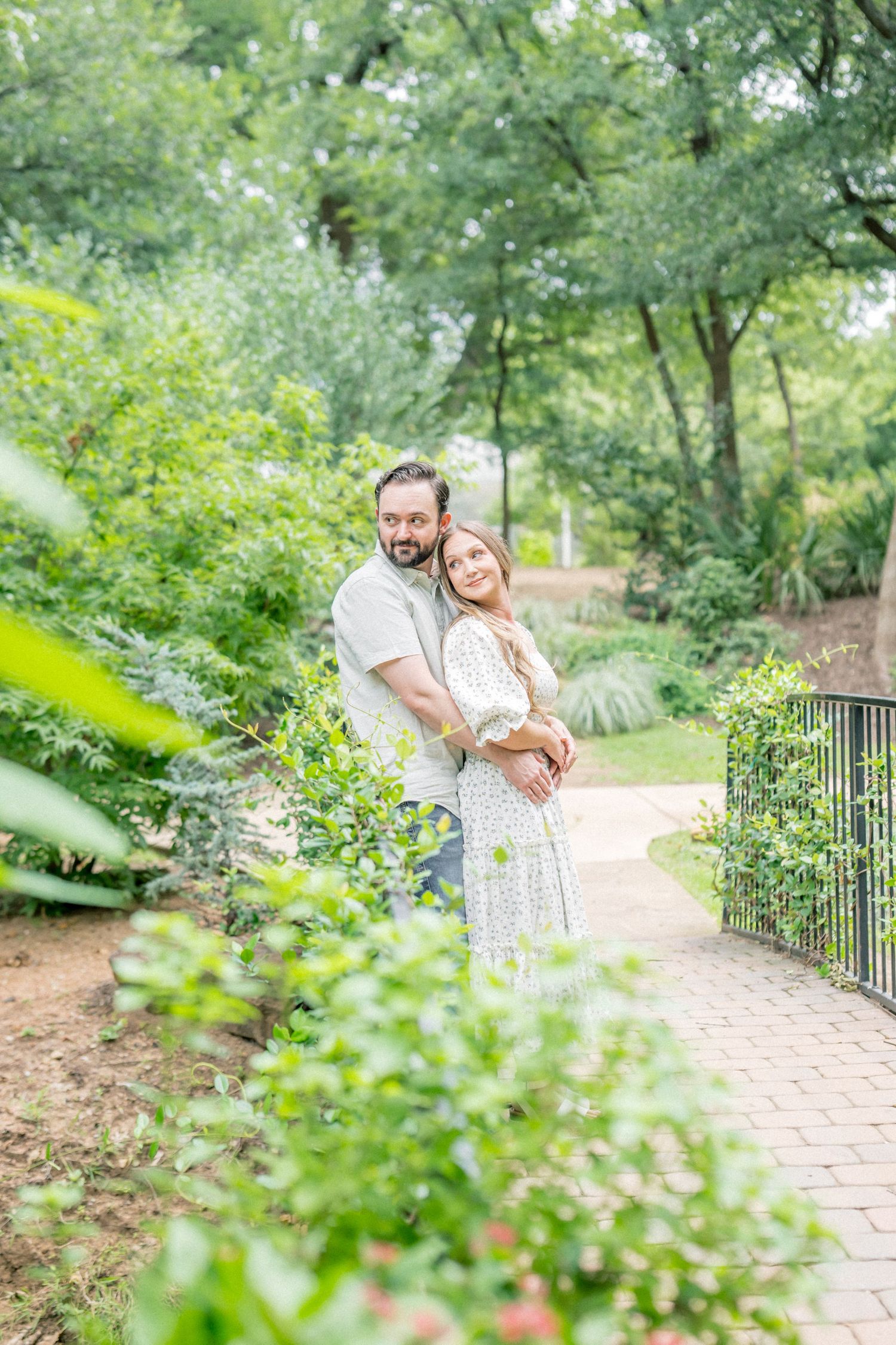 Couple embracing on a garden path surrounded by lush greenery.
