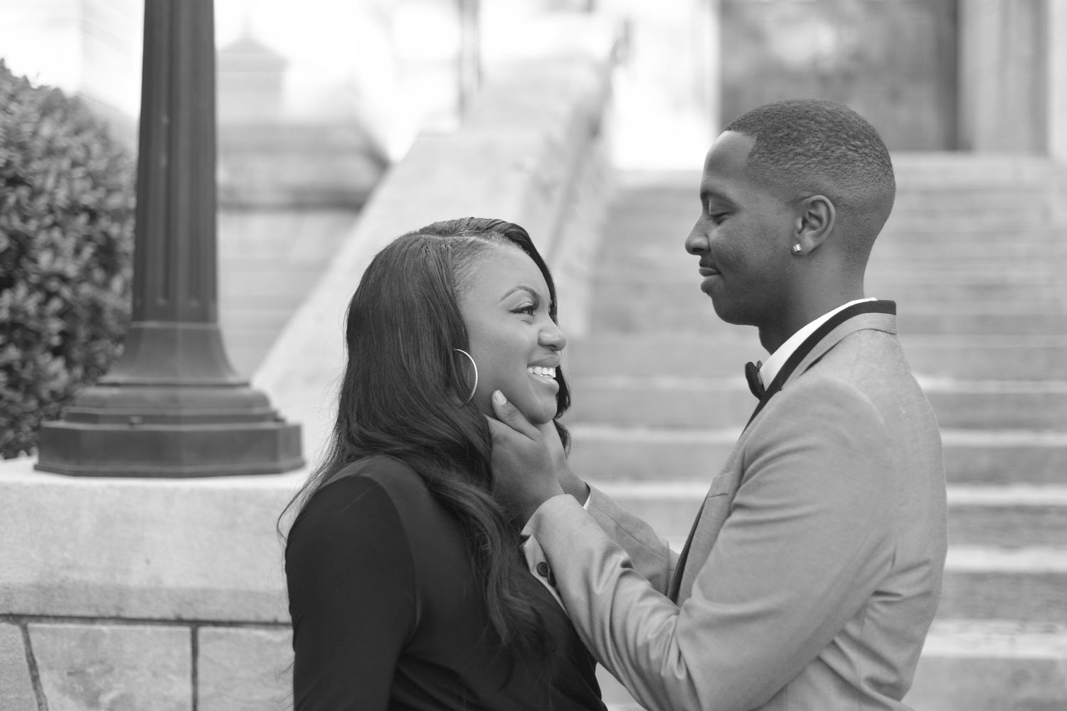 Black and white photo of a couple sharing a tender moment, man gently holding womans face as she smiles.