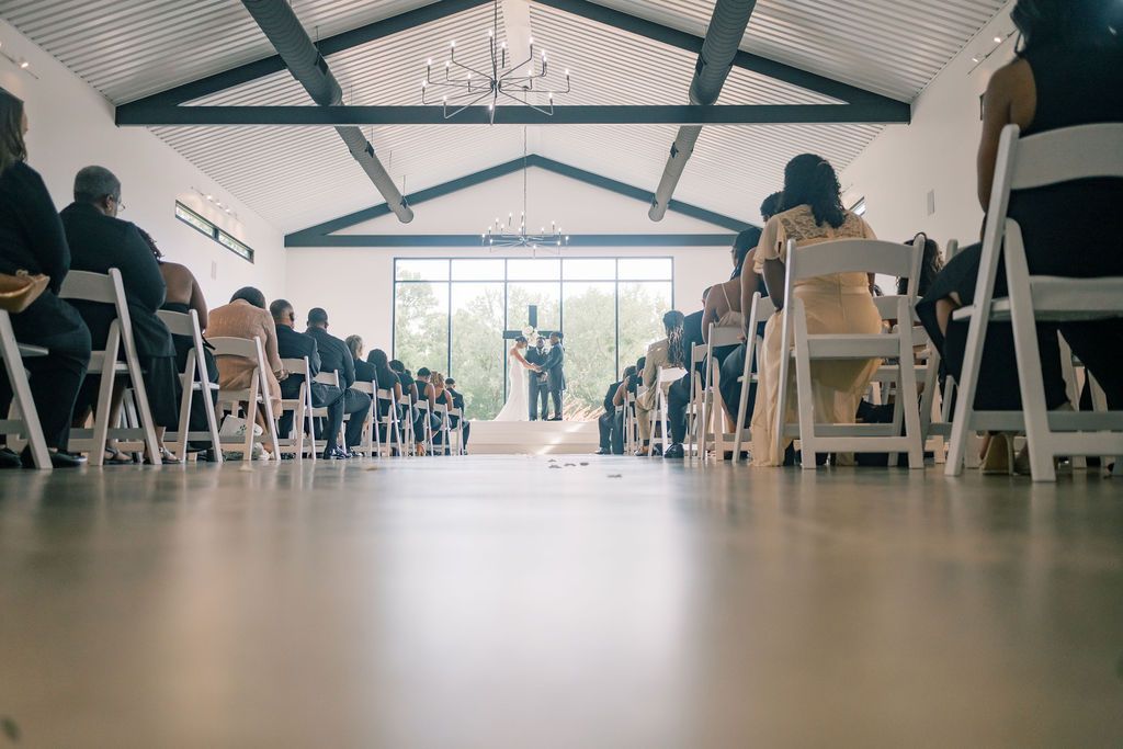 Wide angle view of elegant indoor wedding ceremony aisle with vaulted ceiling and large window backdrop.