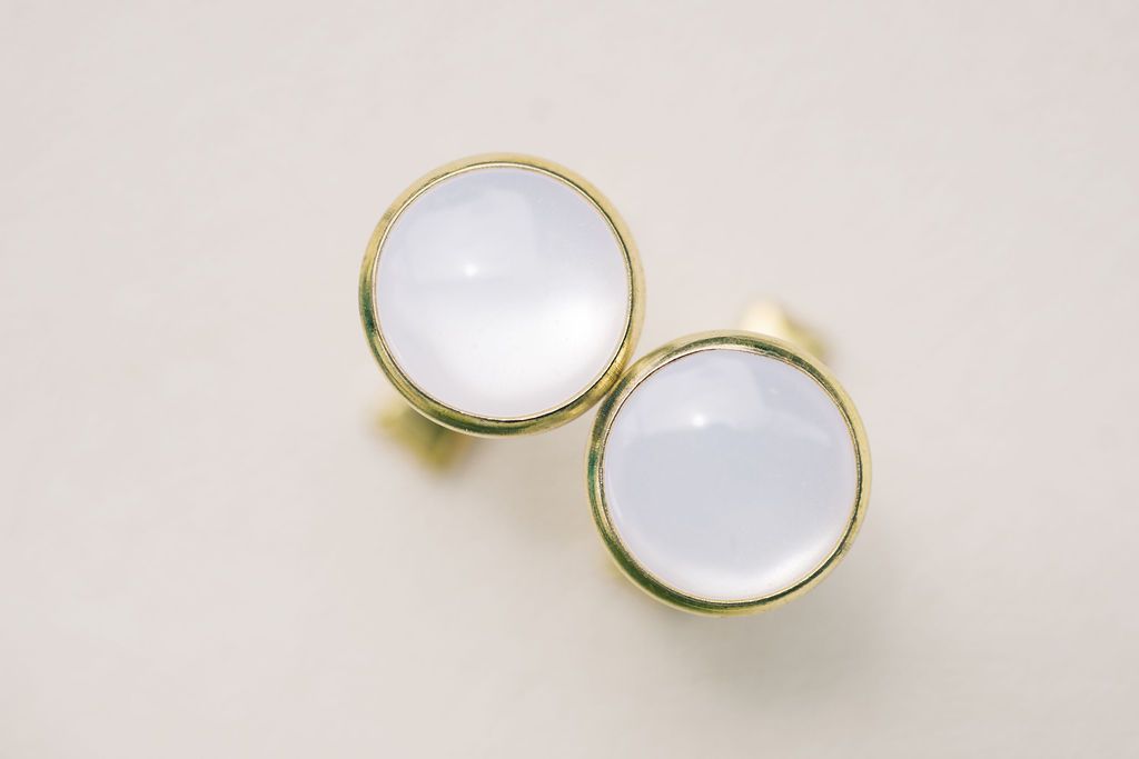 Pair of elegant gold bezel stud earrings featuring smooth round white moonstone cabochons on a neutral background.