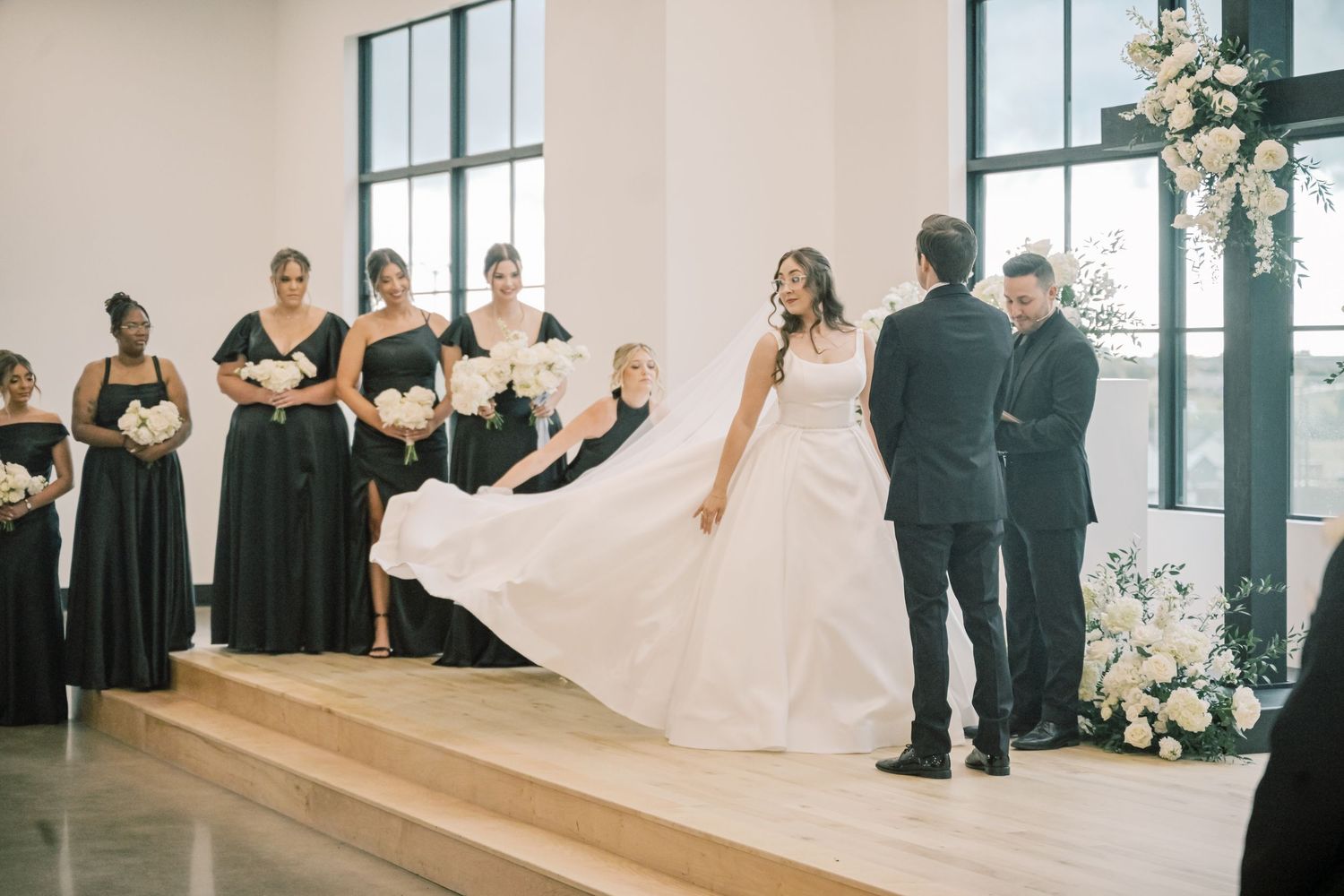 Bride having wedding dress fluffed by bridesmaid at modern wedding ceremony altar.