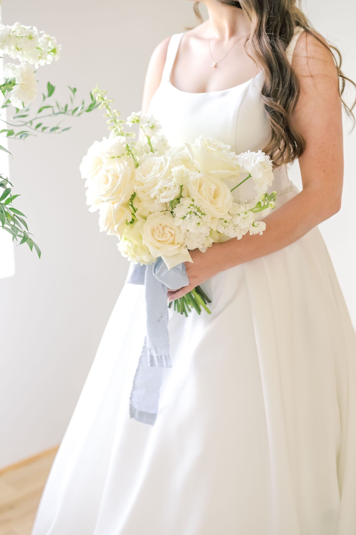 Bride in white wedding gown holding an elegant bouquet of cream roses with gray ribbon.