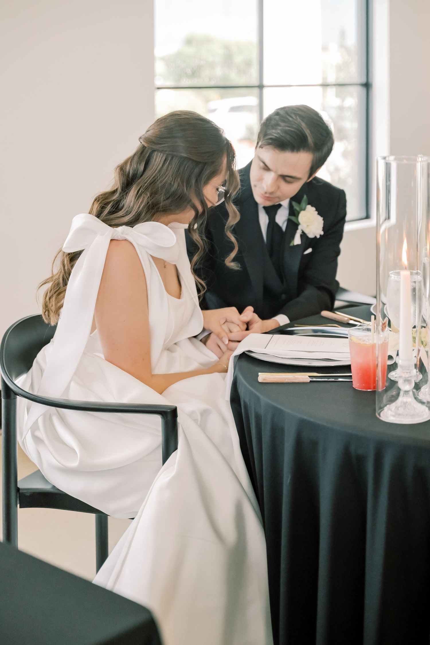 Bride and groom share intimate moment at black draped sweetheart table with candles.