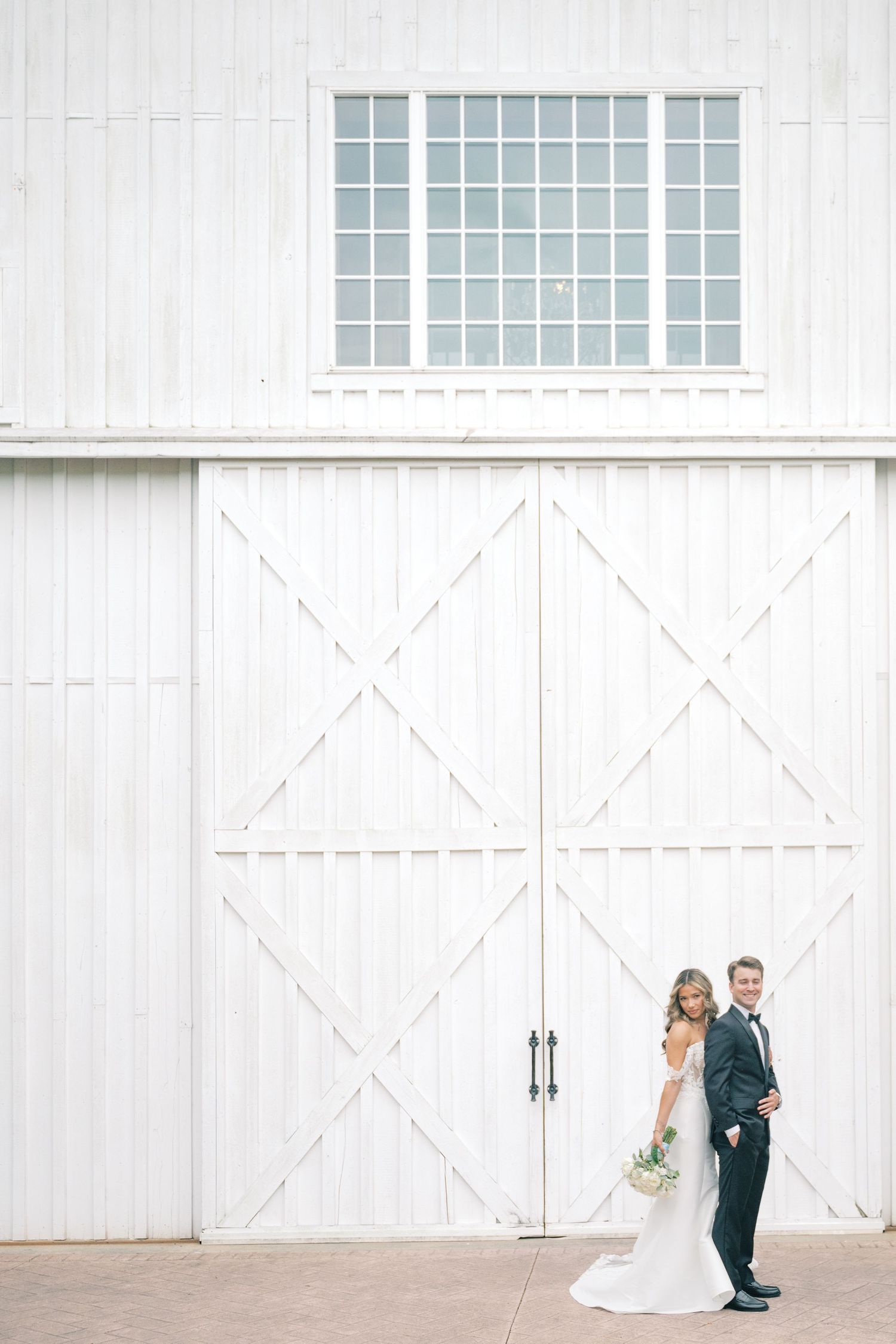 Bride and groom posing together in front of large white barn doors on their wedding day.