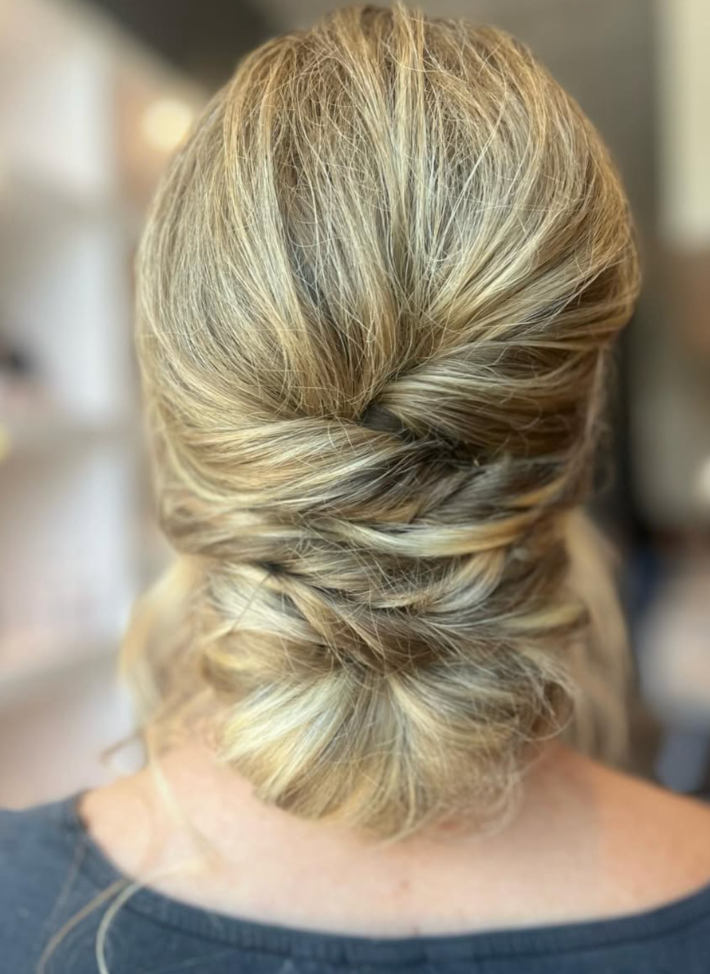 Elegant low updo hairstyle with twisted braid detail and blonde highlights, perfect for weddings or formal events.