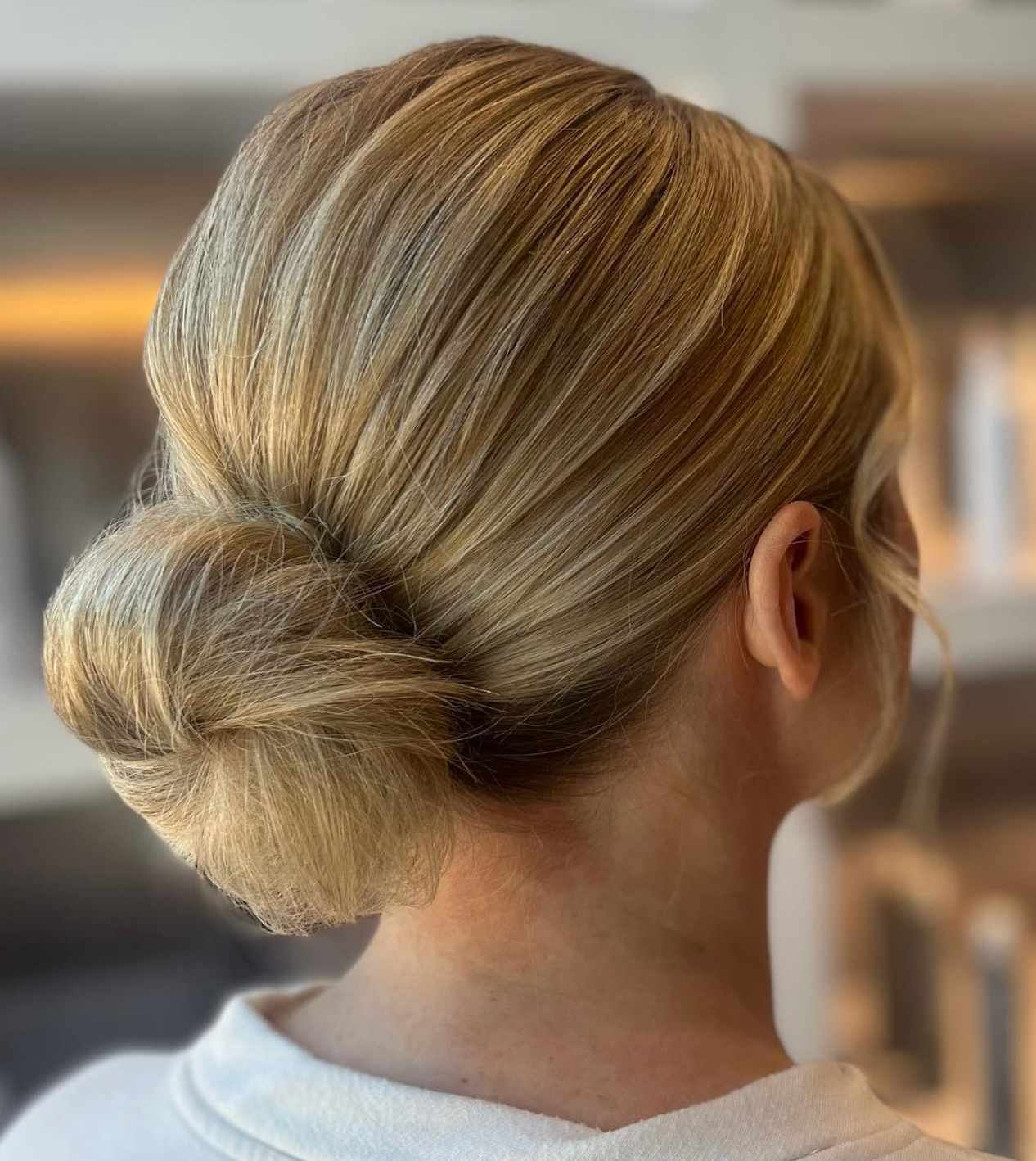 Elegant low bun updo hairstyle with sleek blonde highlights, perfect for weddings or formal occasions.