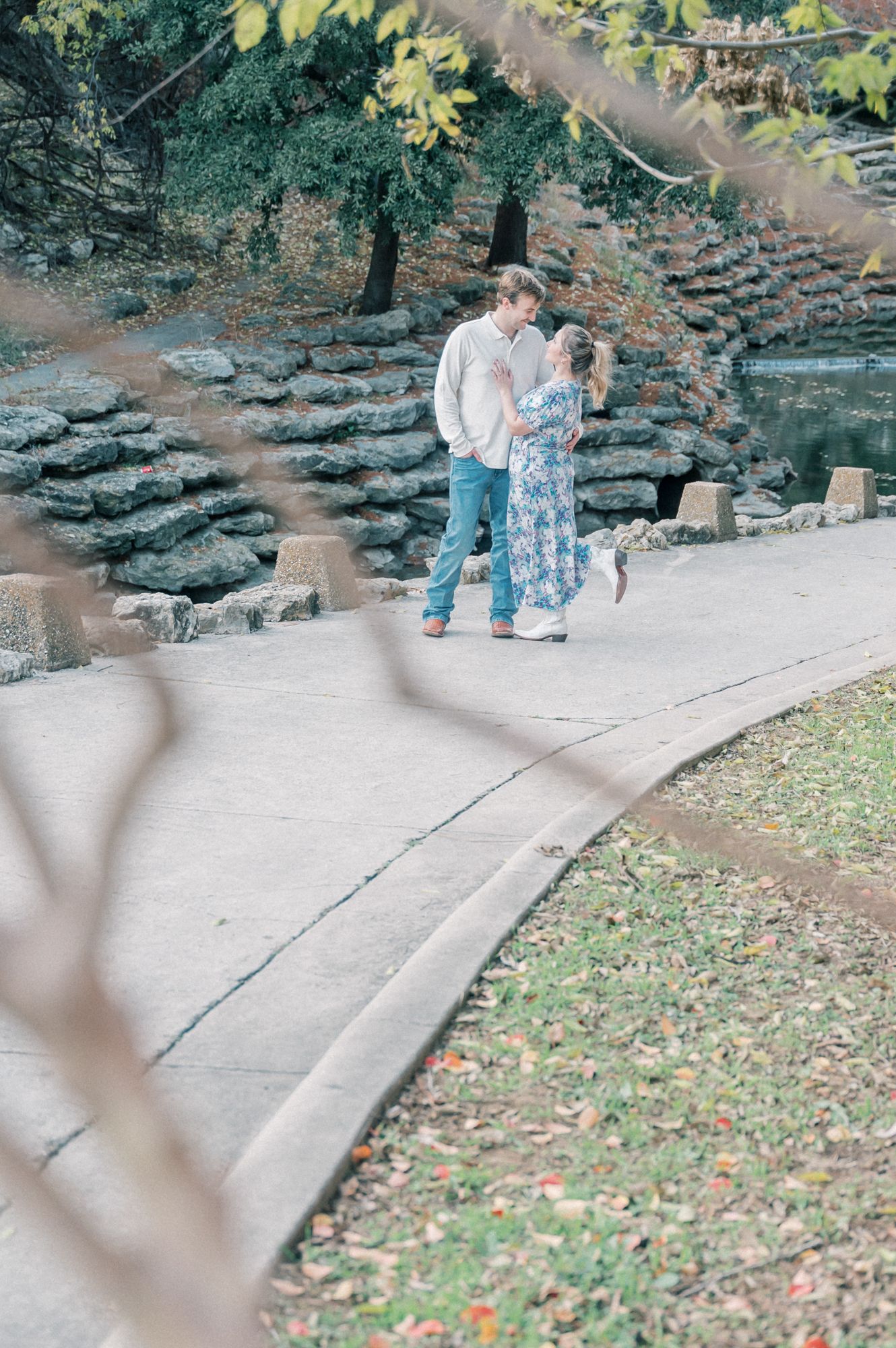 A romantic proposal moment captured on a stone pathway surrounded by autumn foliage and trees.