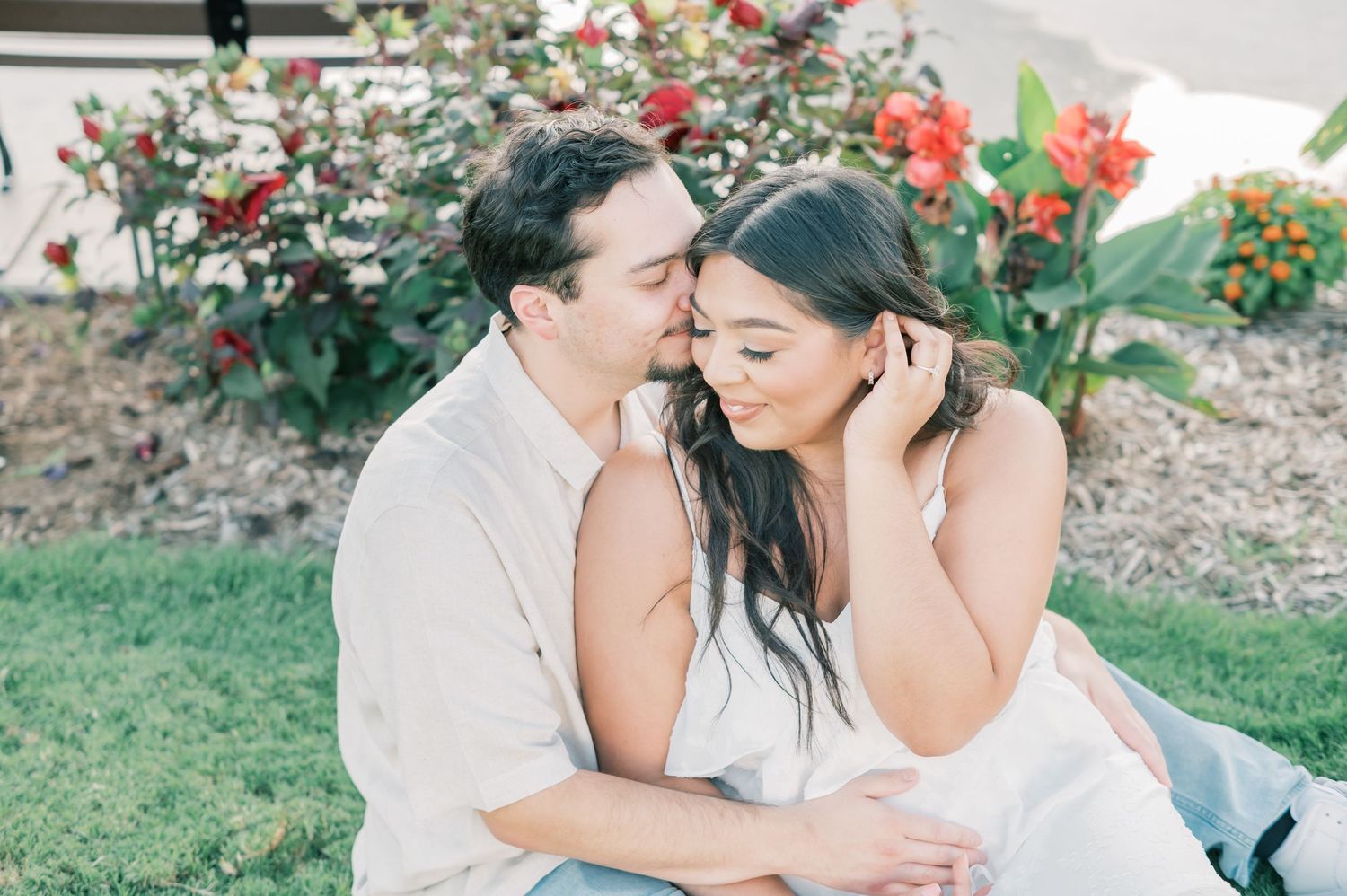 Romantic couple sharing tender moments in a garden setting with red flowers in the background.