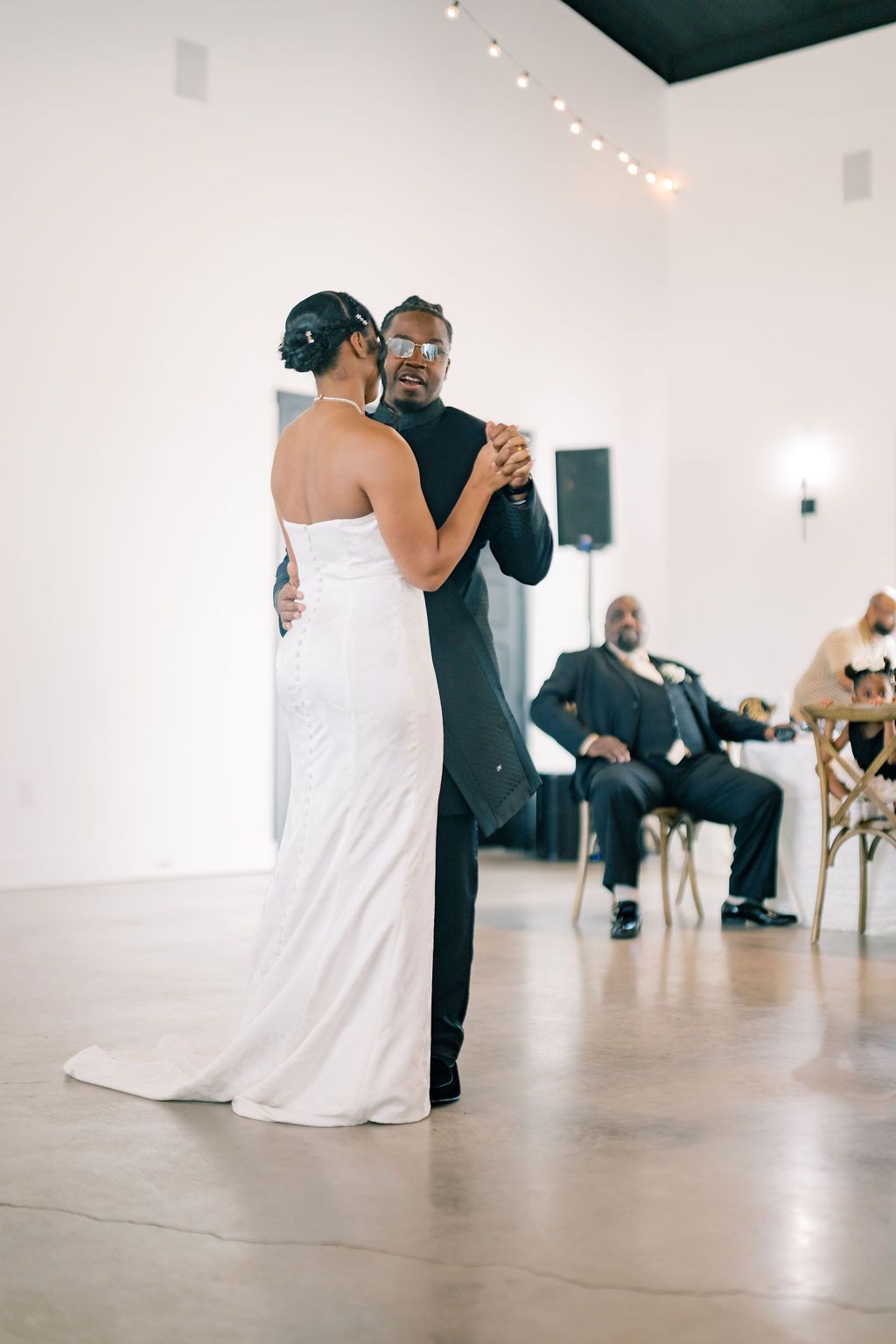 Bride and groom share their first dance at wedding reception in white venue.