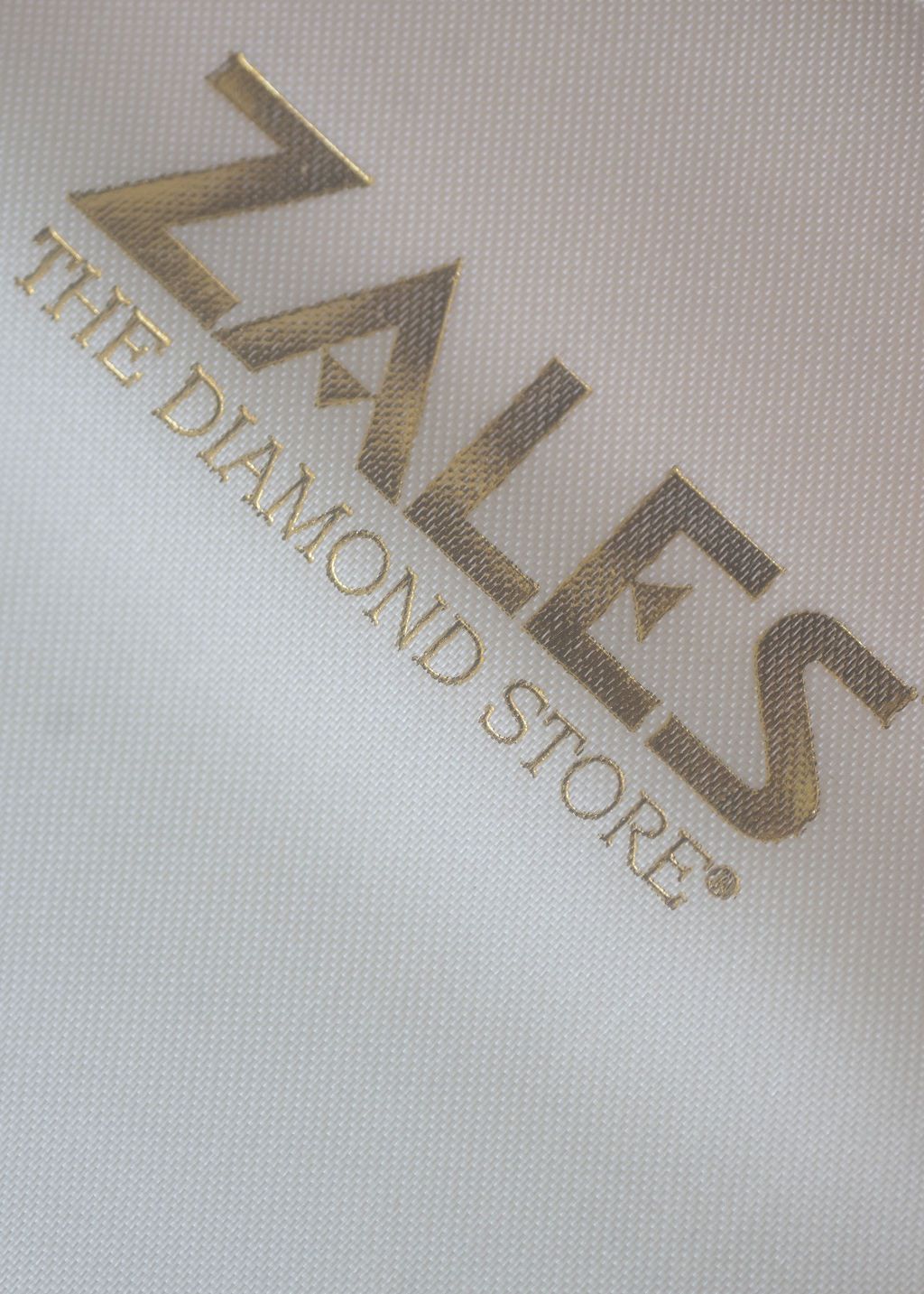 Zales The Diamond Store logo embossed in gold on white textured fabric background.