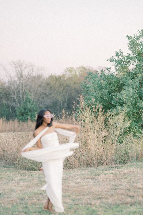 Ethereal movement captured in white dress among wild grasses and trees at sunset.