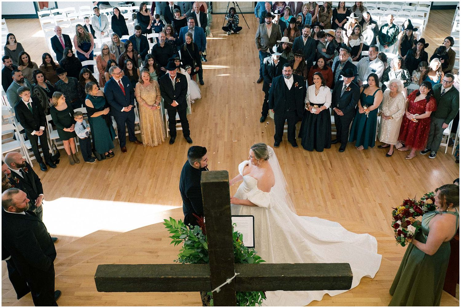 Large wedding ceremony in progress with guests seated in rows watching the proceedings on a wooden floor.