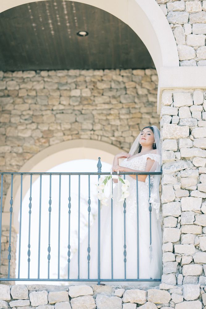 A person lies on a stone balcony with arched windows and blue railings in a dreamy architectural setting.