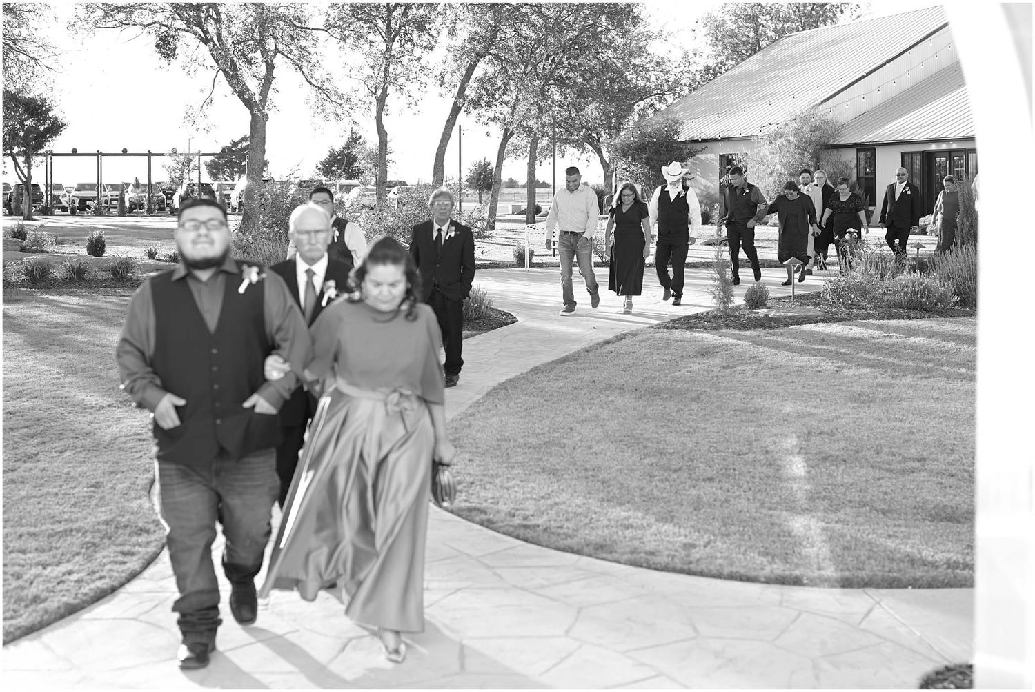 Black and white photo of wedding guests walking on outdoor pathway.