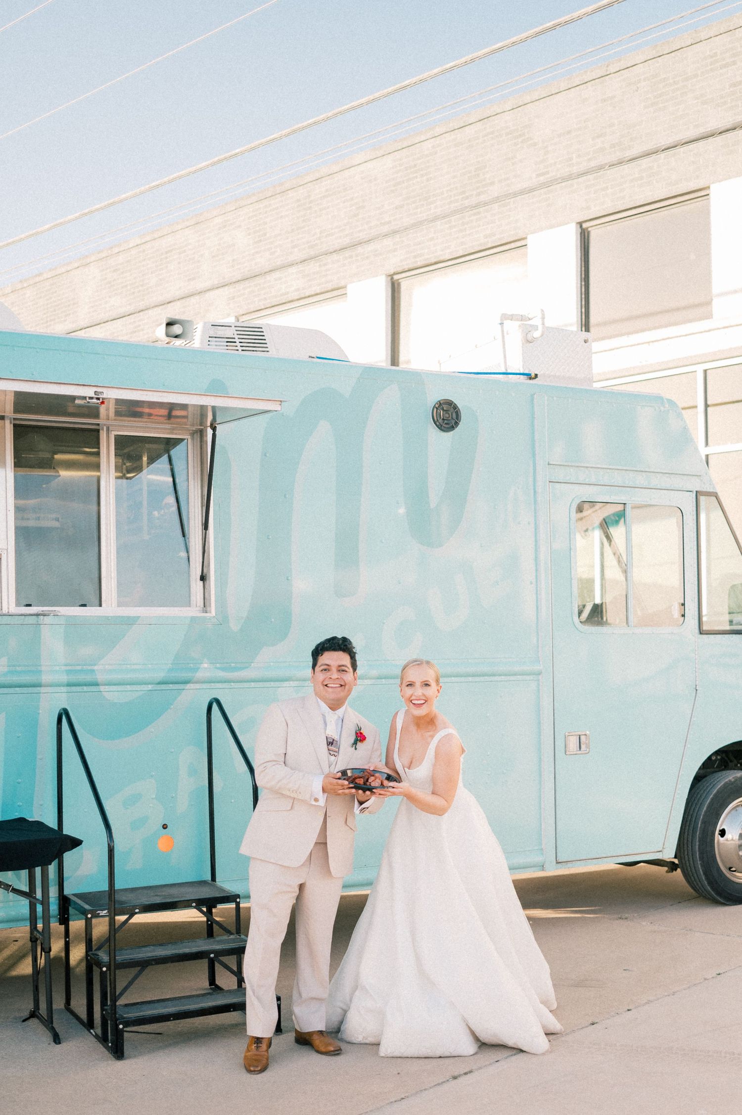 Wedding couple poses in front of a mint blue food truck in formal attire.