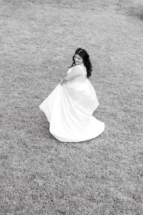 Bride in white gown twirling on grass in black and white photo.