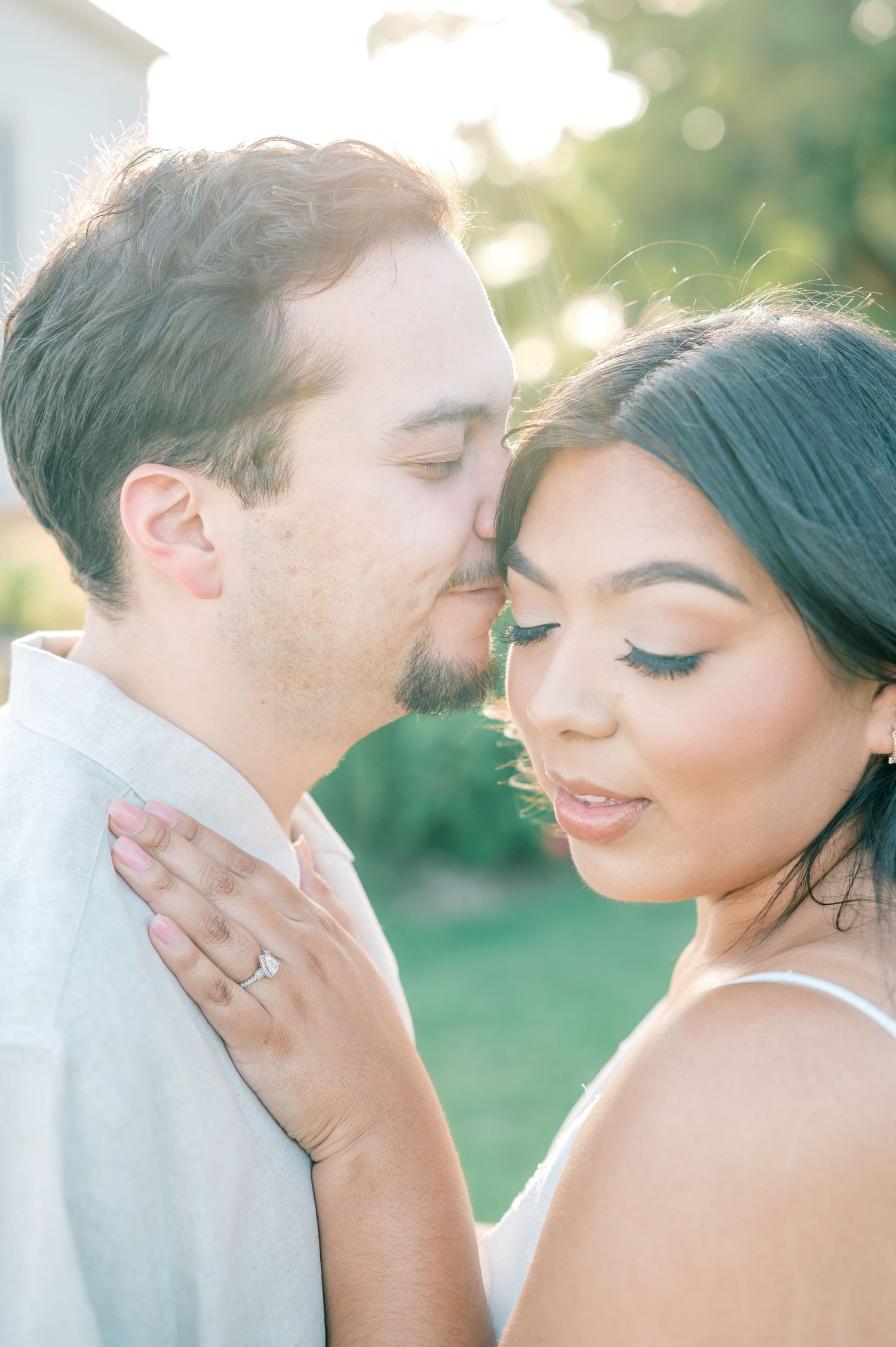 Romantic wedding couple shares intimate moment in sunlit garden setting with soft bokeh background.
