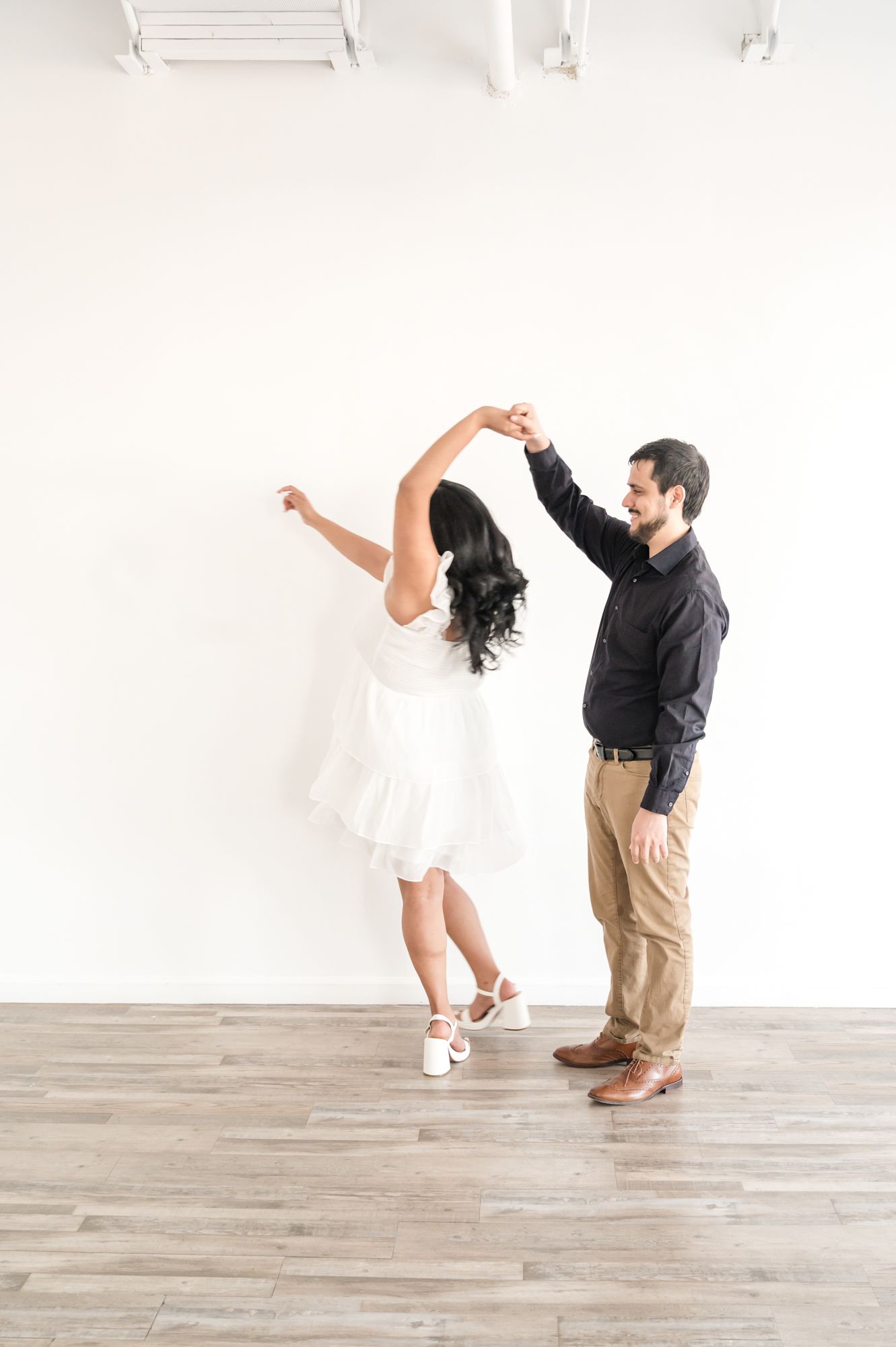 A couple dances together in a bright minimalist room with white walls and wooden floors.