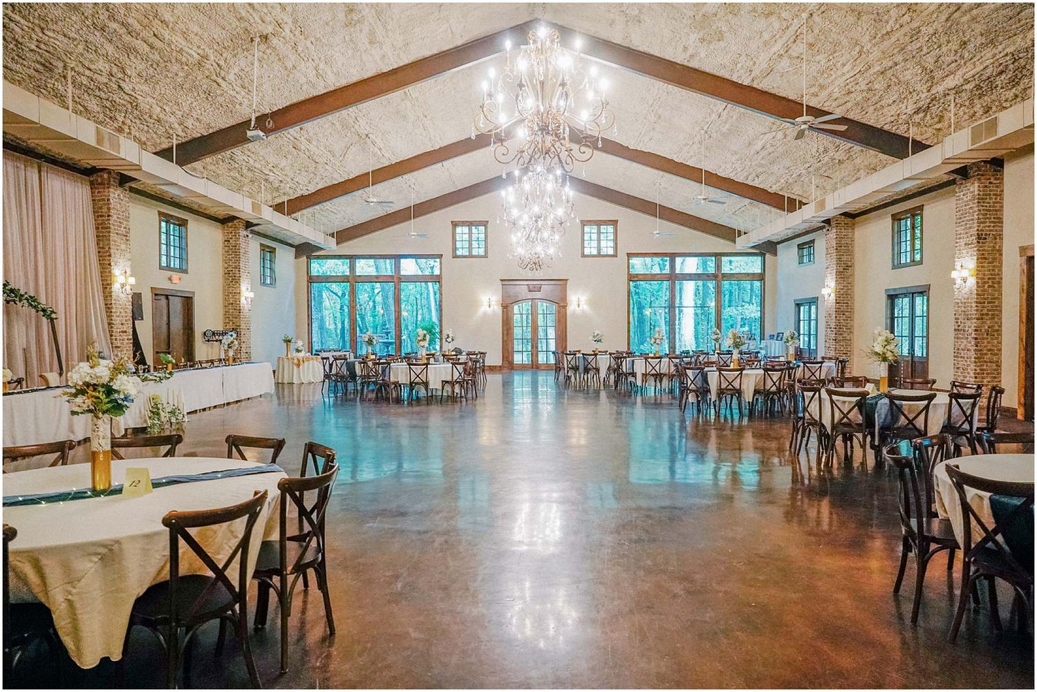 Rustic wedding reception hall with exposed brick walls, chandeliers, and round tables elegantly set.