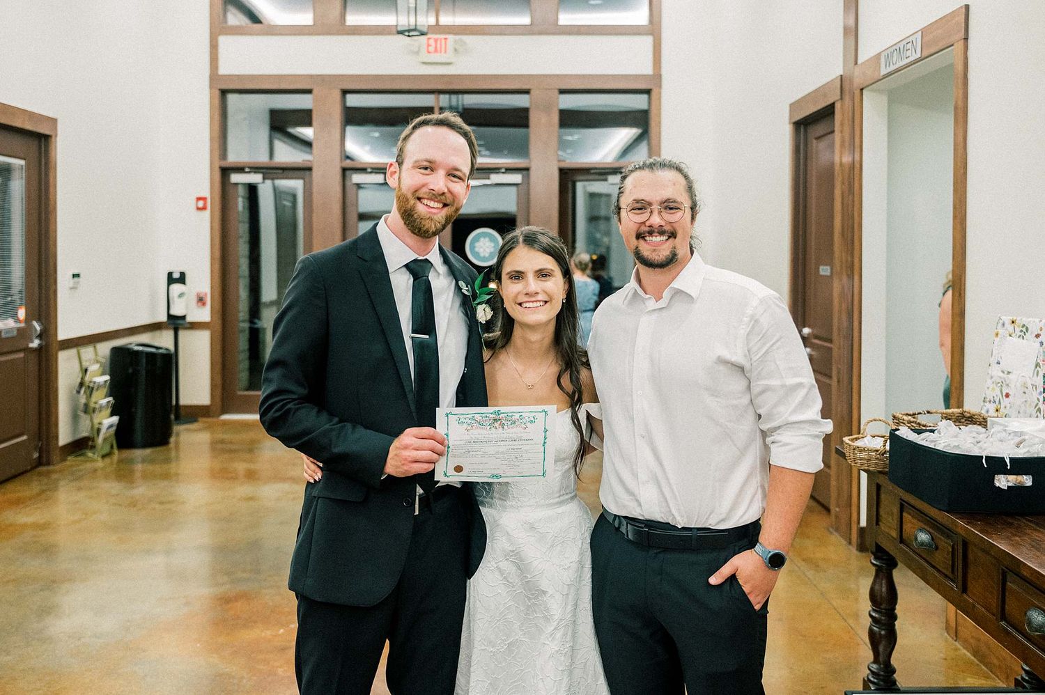 Newlyweds celebrating with a guest while holding a marriage certificate in an elegant venue.