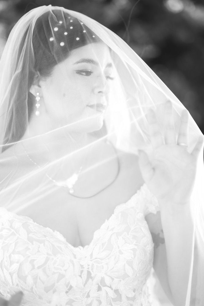 Black and white portrait of bride beneath dotted veil with romantic expression.