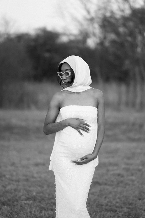 Black and white maternity portrait with stylish sunglasses and flowing white fabric.