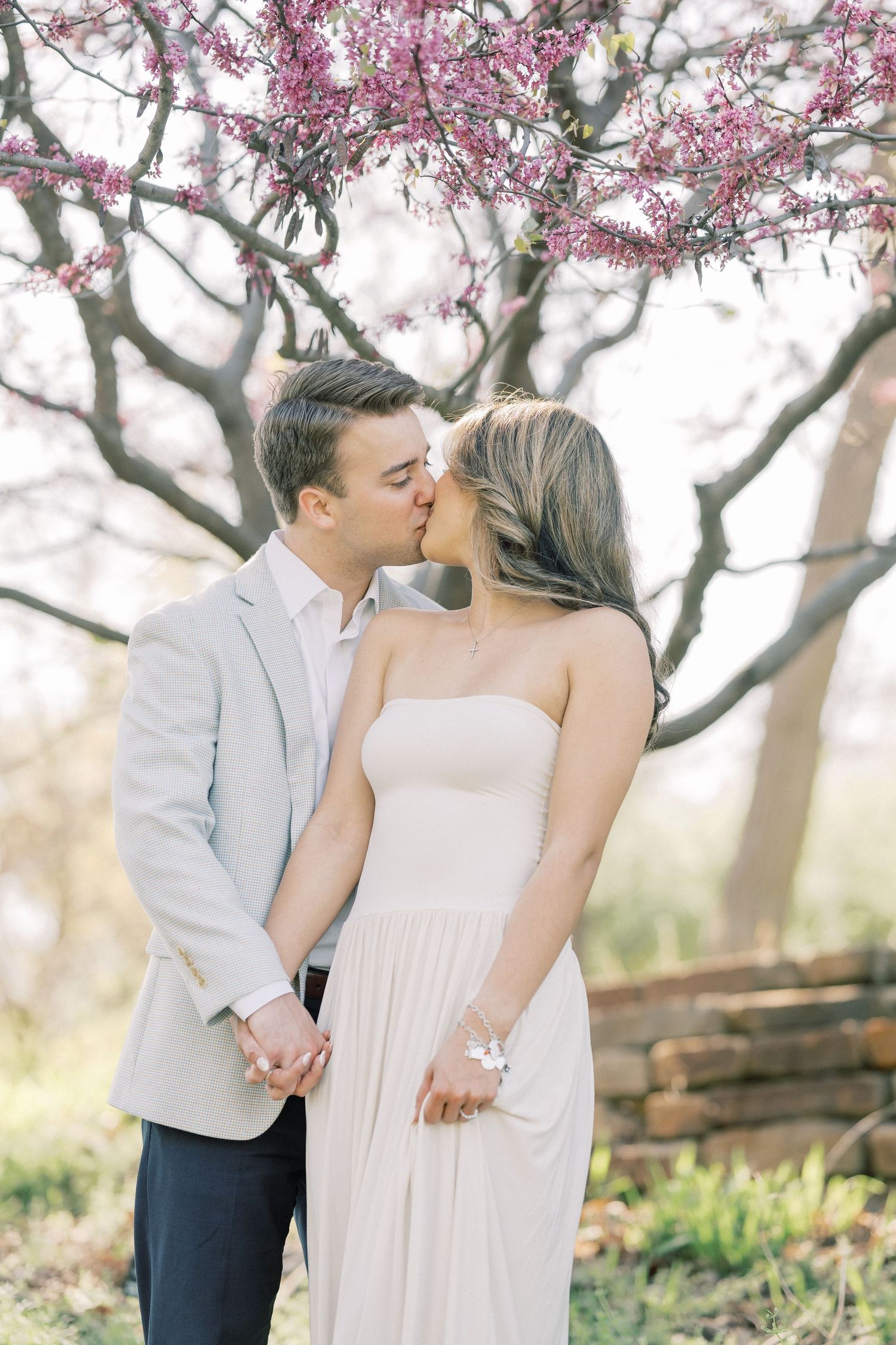 A romantic spring moment under blooming cherry blossom trees as a couple shares a tender kiss in a garden setting.