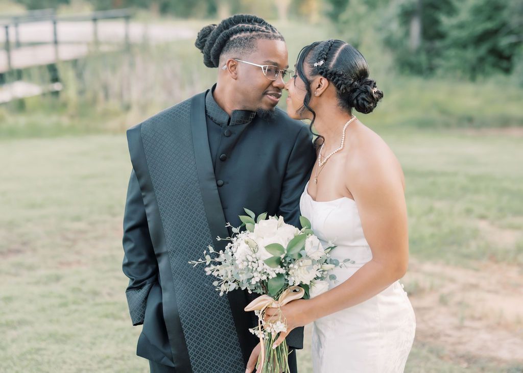 Newlywed couple sharing a romantic moment outdoors, bride holding white bouquet in elegant white gown.