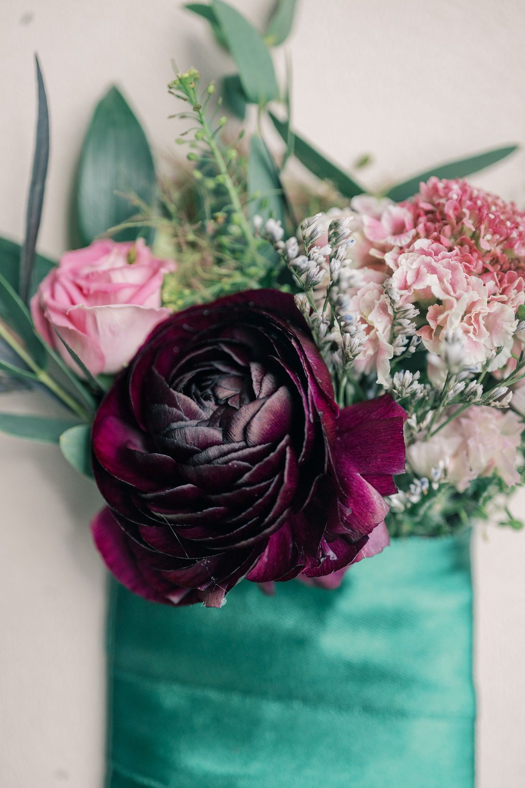 Deep purple ranunculus with pink roses and greenery arranged in a teal vase, elegant floral bouquet.