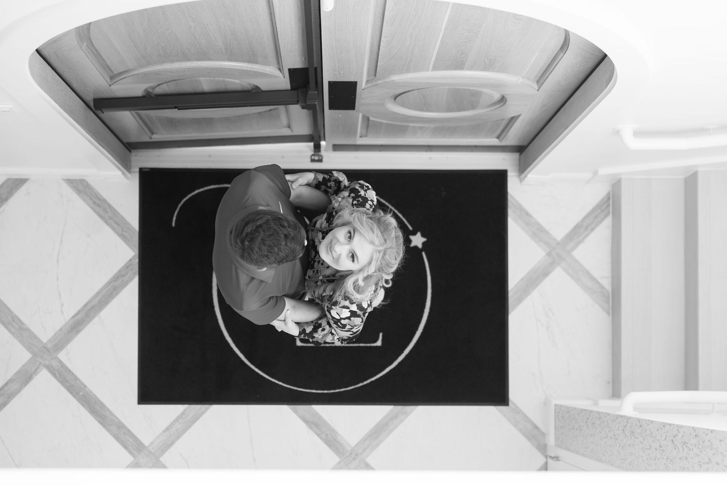 Aerial black and white view of couple embracing on a decorative floor pattern.