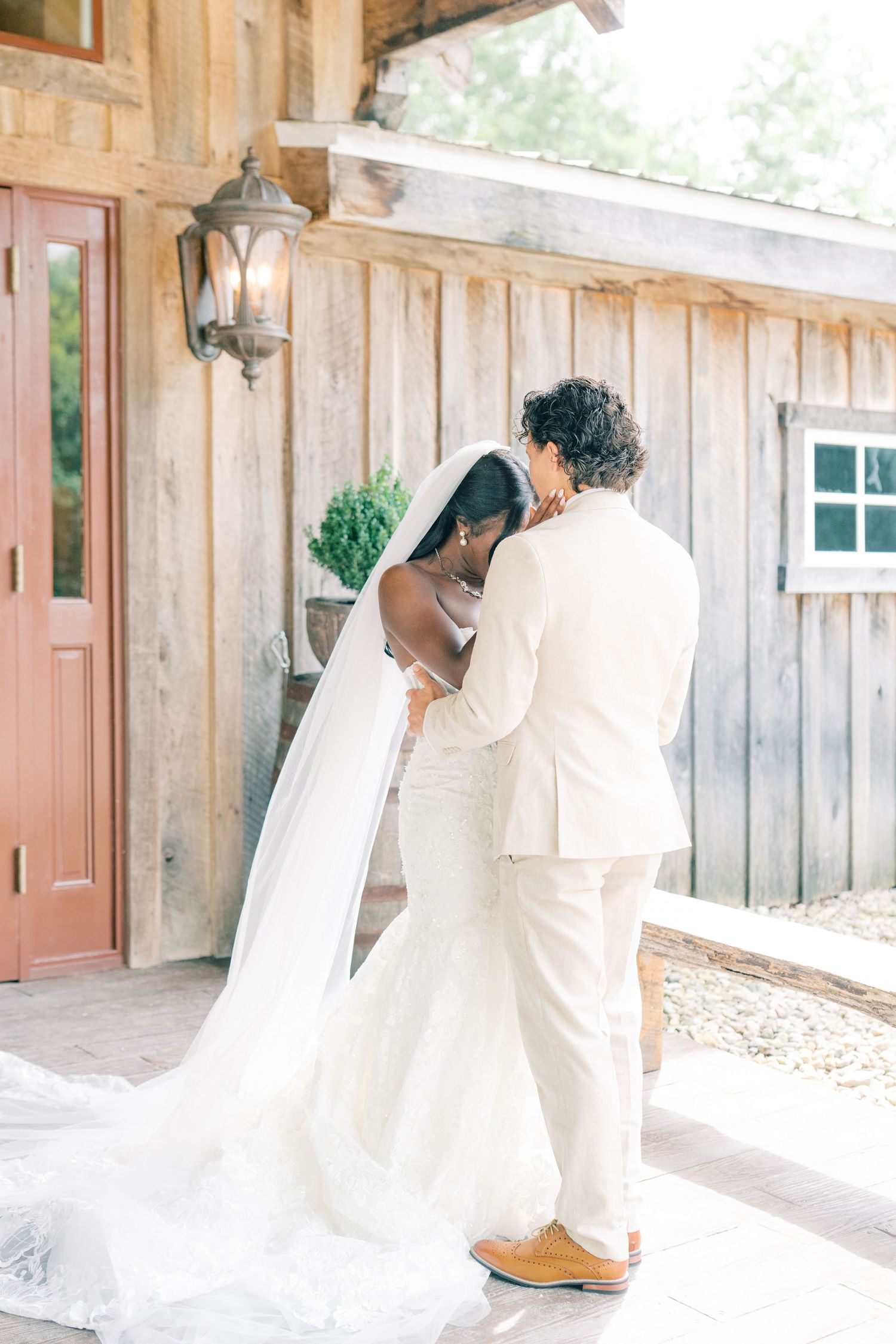 Bride and groom share tender first look moment outside rustic wooden barn venue on their wedding day.
