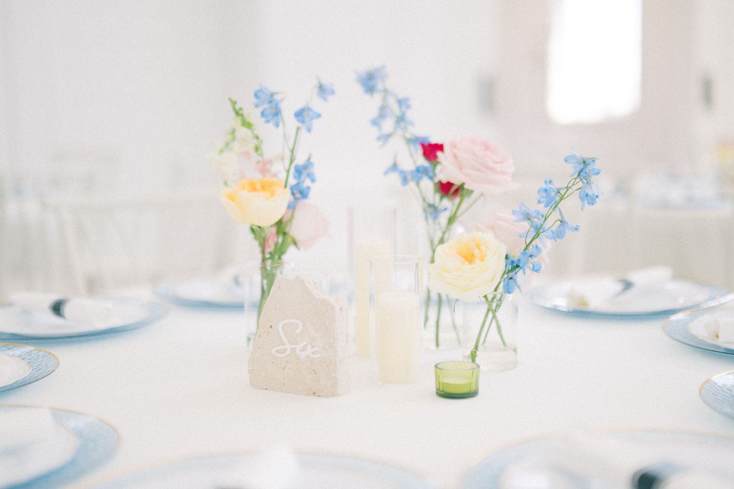 Elegant wedding reception table with blue and pink floral centerpieces, candles, and light blue place settings.