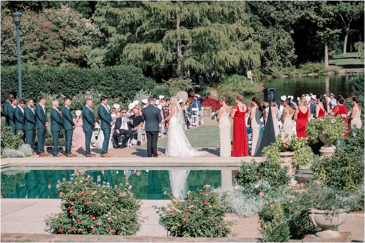 Wedding party and guests lined up for photos along a garden pool with colorful attire.