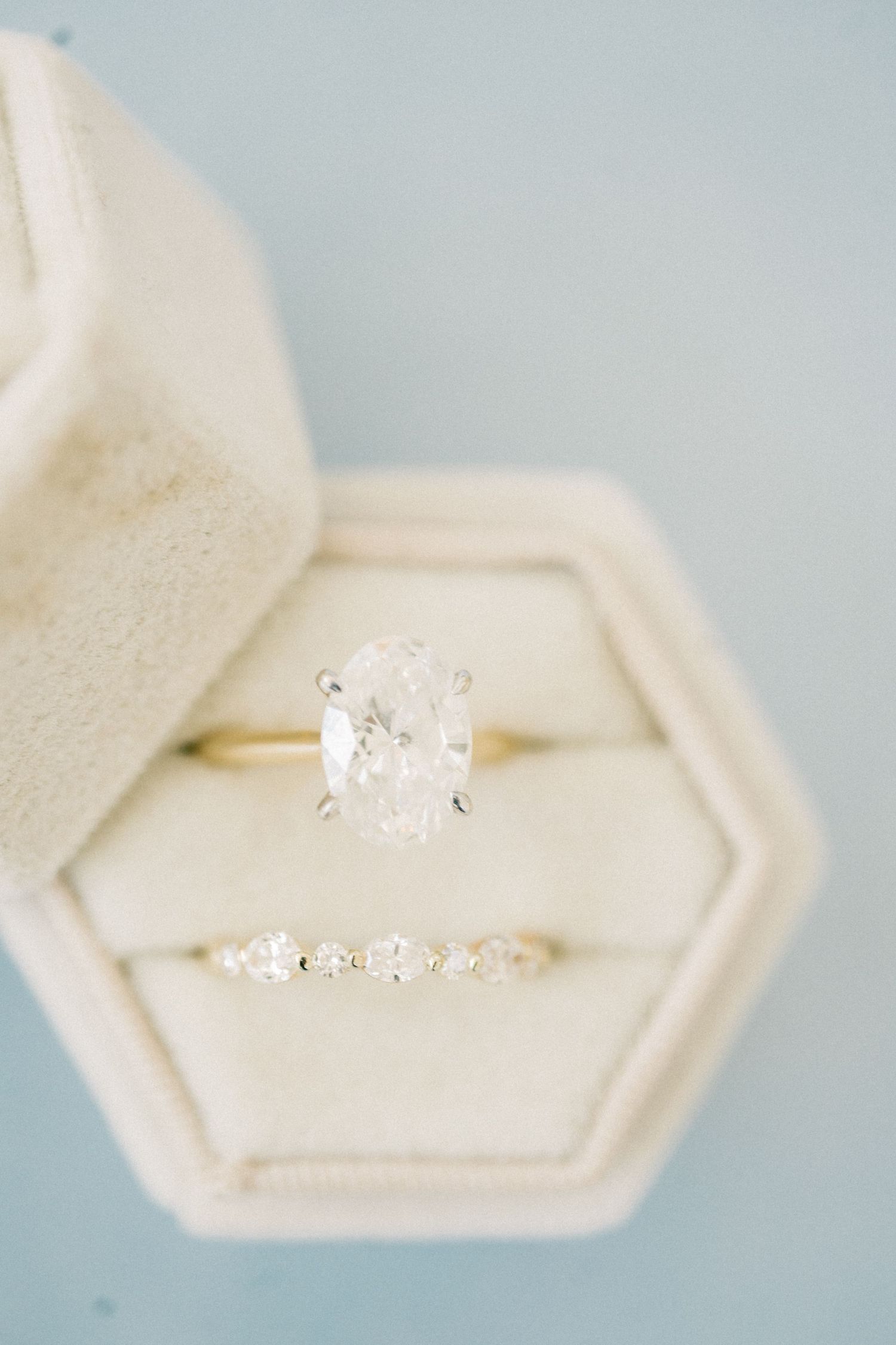 Oval diamond solitaire engagement ring and delicate diamond band displayed in a hexagonal velvet ring box.