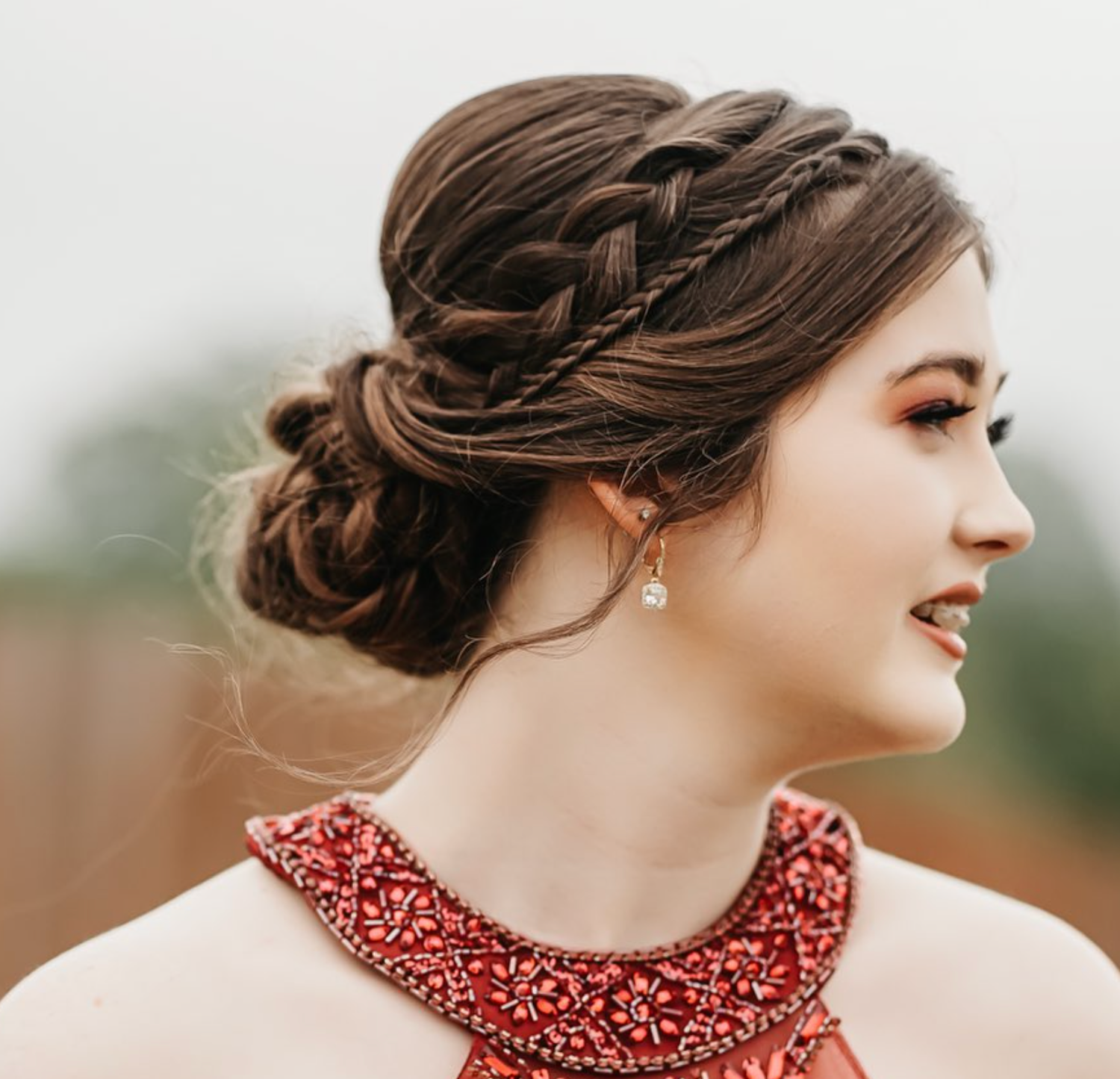 Young woman with elegant braided updo hairstyle wearing a red beaded dress and pearl drop earrings.
