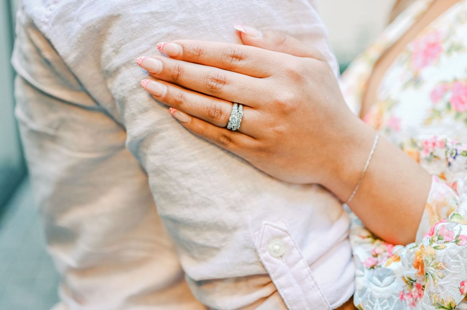 Close-up of a womans hand with a diamond engagement ring resting on a mans arm.