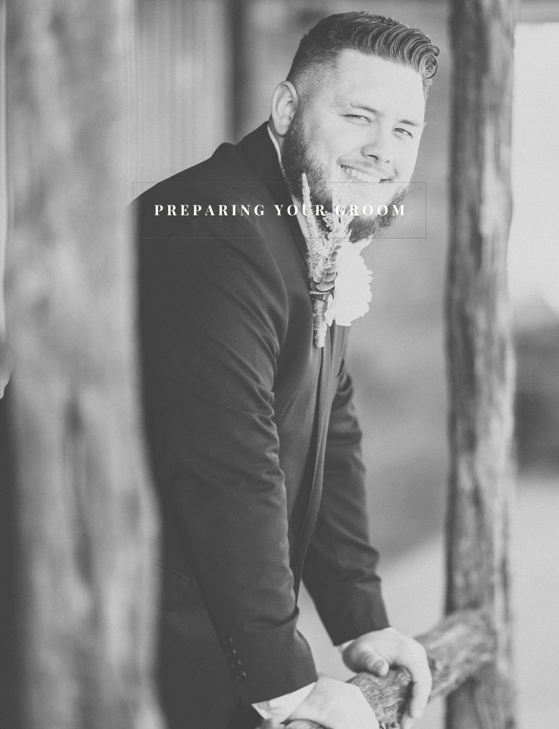 Smiling groom in black suit with boutonniere posing outdoors in black and white wedding photo.